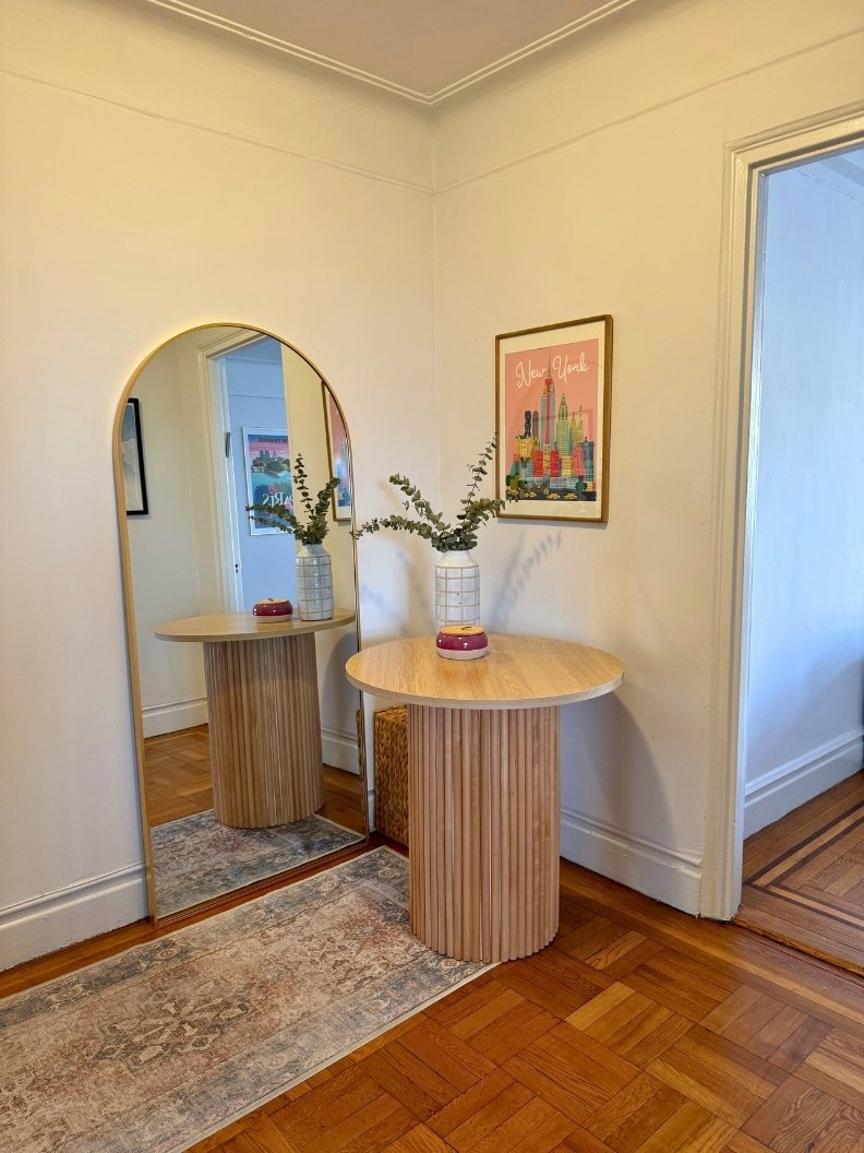 Entryway with a vintage coral and blue runner, a wooden round table, a large golden arched floor mirror, and artwork on the wall. Styled with a handmade pottery vase and dried eucalyptus.