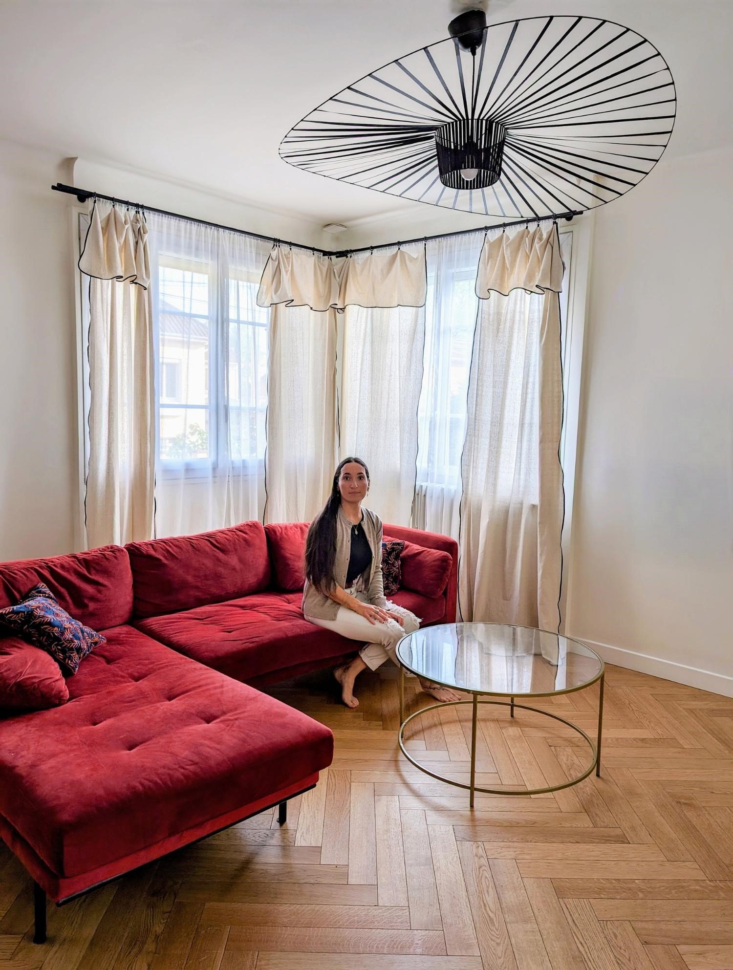 L'Atelier By ATB designer, Alice, seated in a bright and airy Parisian minimalist living room with herringbone light oak hardwood floors.