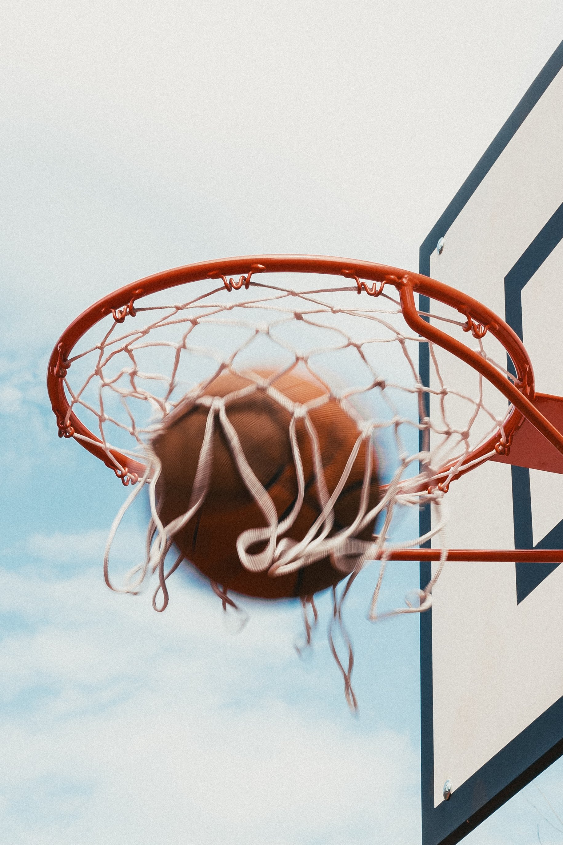 Close-up of a basketball going through a basketball hoop on an outdoor court with a blue sky background.