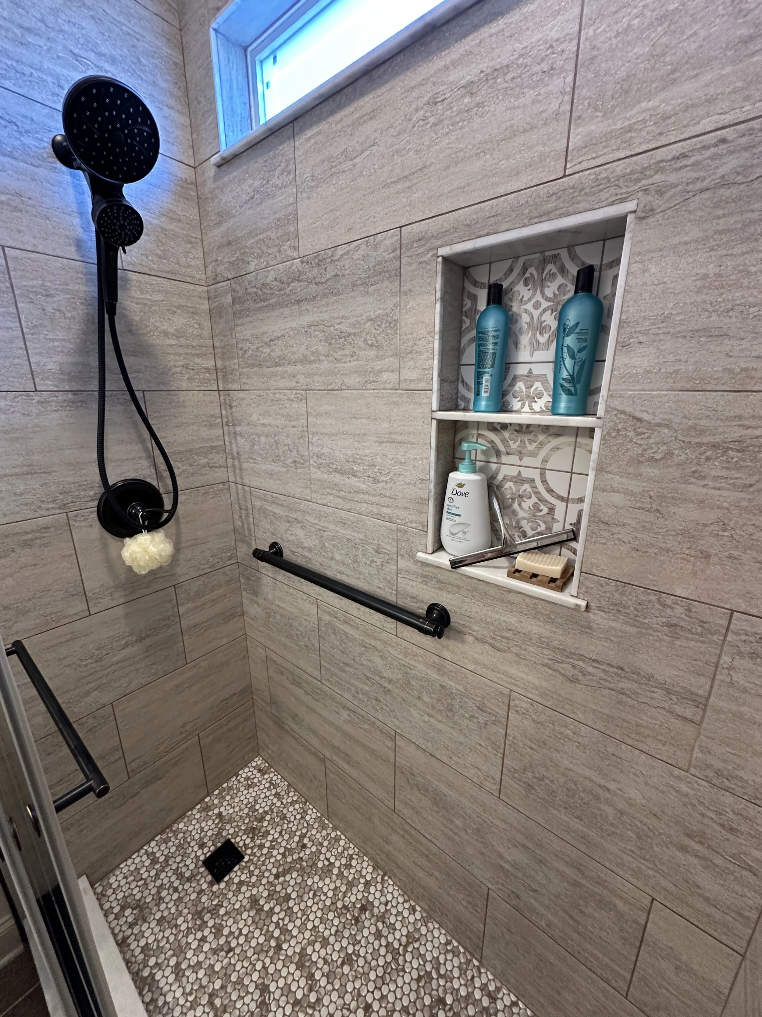 Custom tile shower interior with built-in niche, decorative accent tile, penny mosaic floor, and matte black fixtures — Centerline Construction