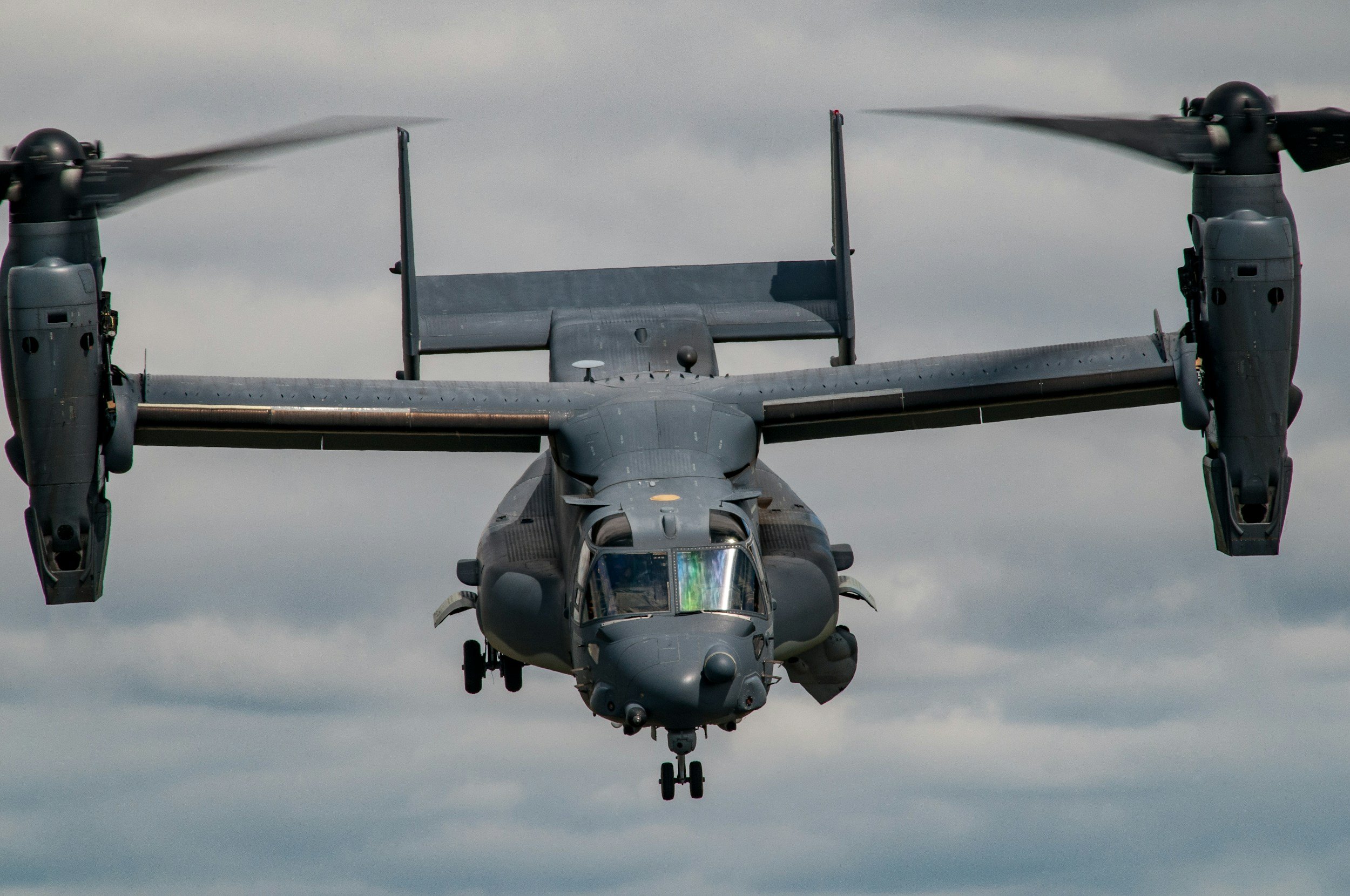 A military V-22 Osprey aircraft flying in cloudy skies.