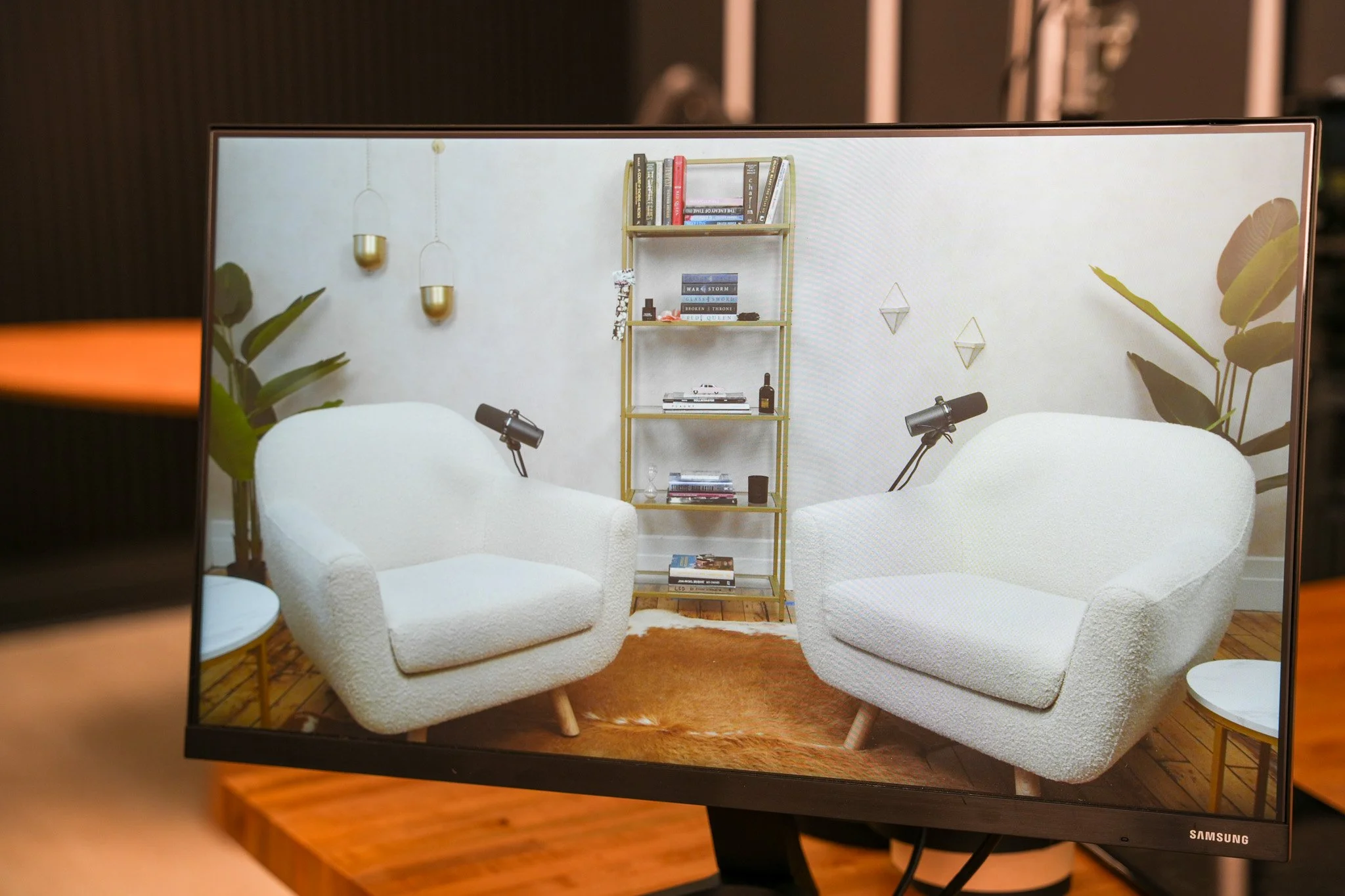 A computer monitor displaying a cozy living room setup with two white armchairs, small side tables, a gold bookshelf with books and decor, plants, and wall decorations.