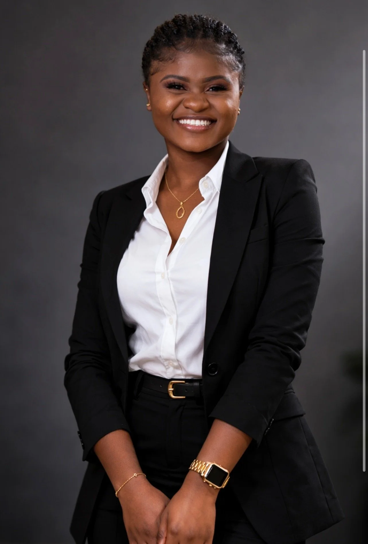 A man in a black pinstripe suit, blue shirt, and patterned tie smiling for a professional photo in front of a blurred background with text and logos.