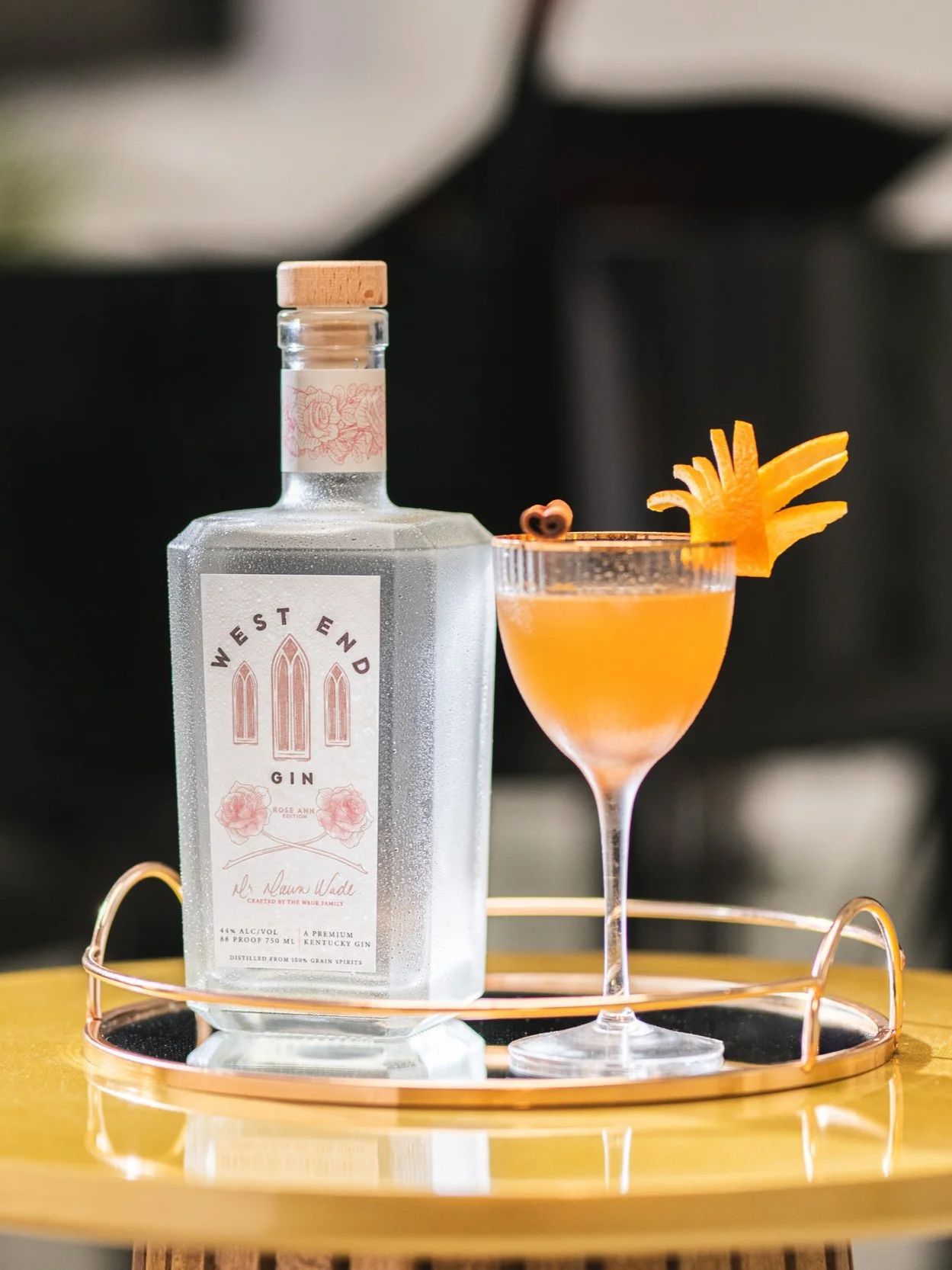 Orange cocktail in a cocktail glass on a serving tray with a square gin bottle