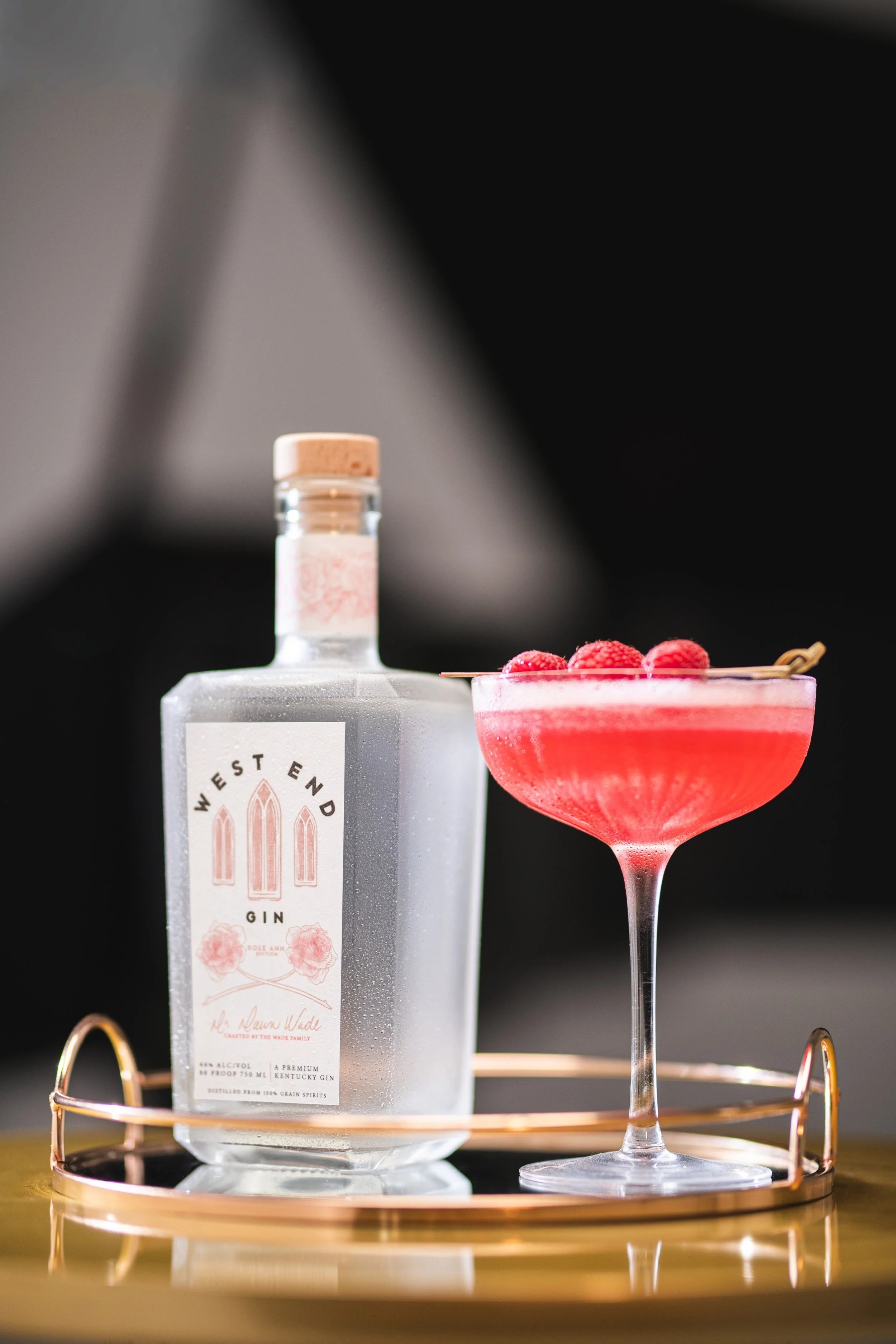 Pink cocktail in a coupe glass on a serving tray with a square gin bottle