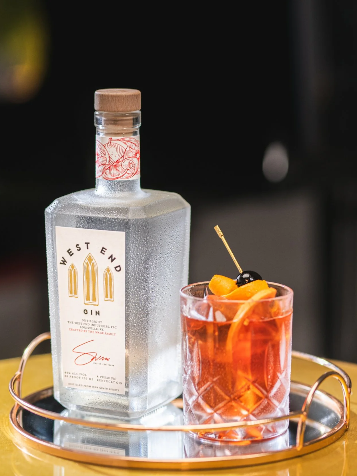 Elegant cocktail with orange and brandied cherry garnish on a serving try with a square gin bottle