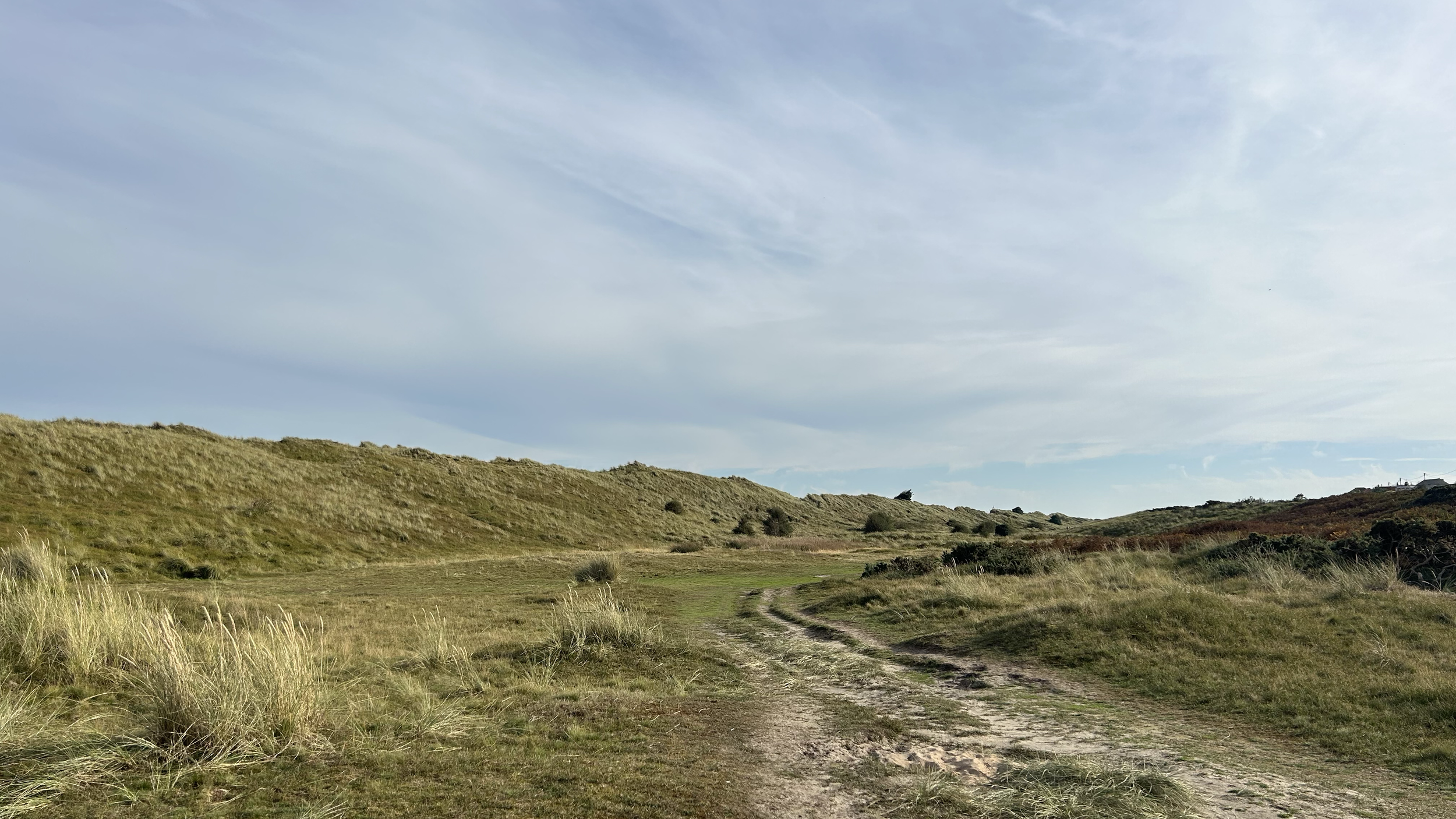 A dirt path winding through grassy rolling hills under a partly cloudy sky.