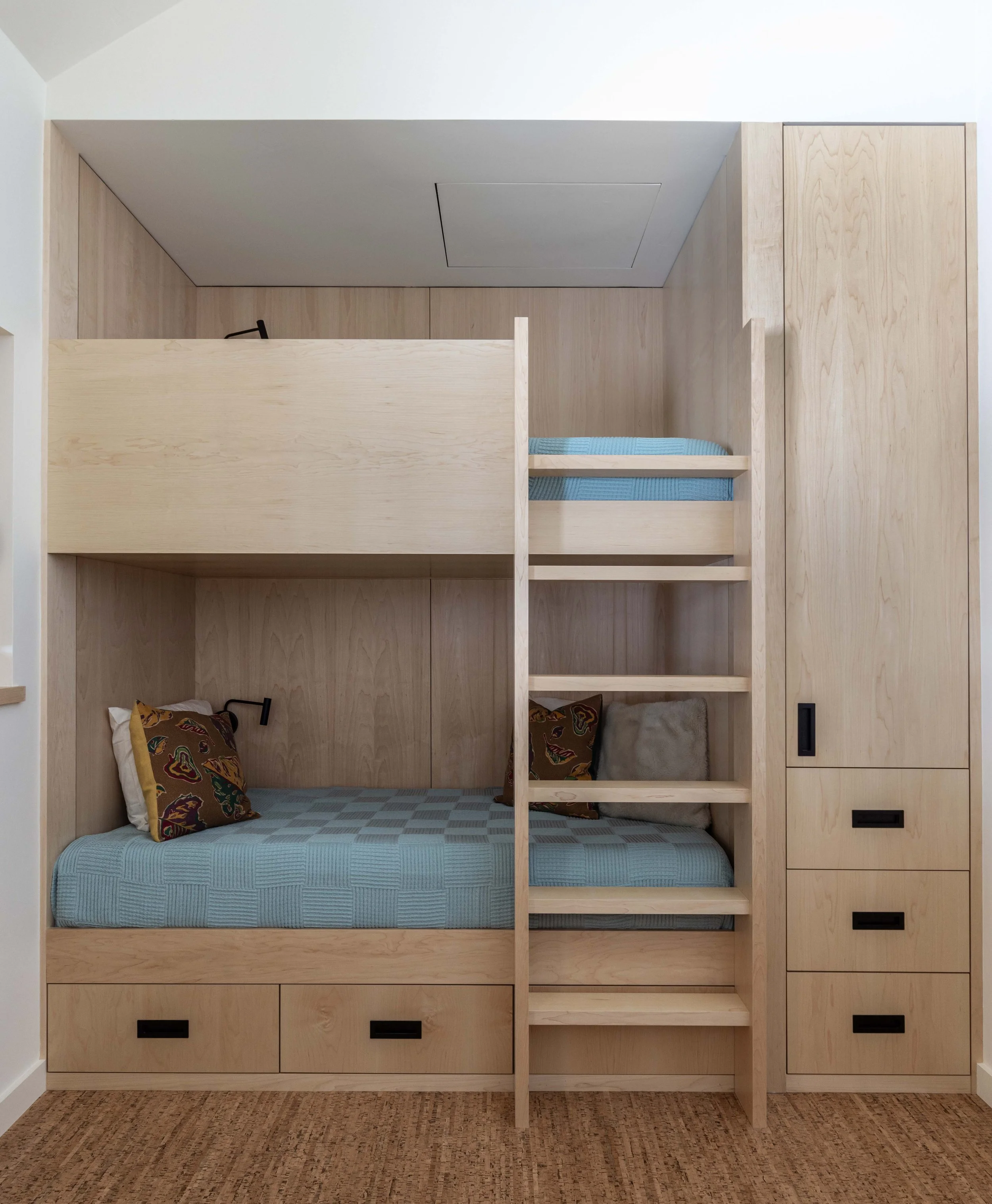 Wooden bunk bed with storage drawers and a ladder, featuring blue bedding and decorative pillows.