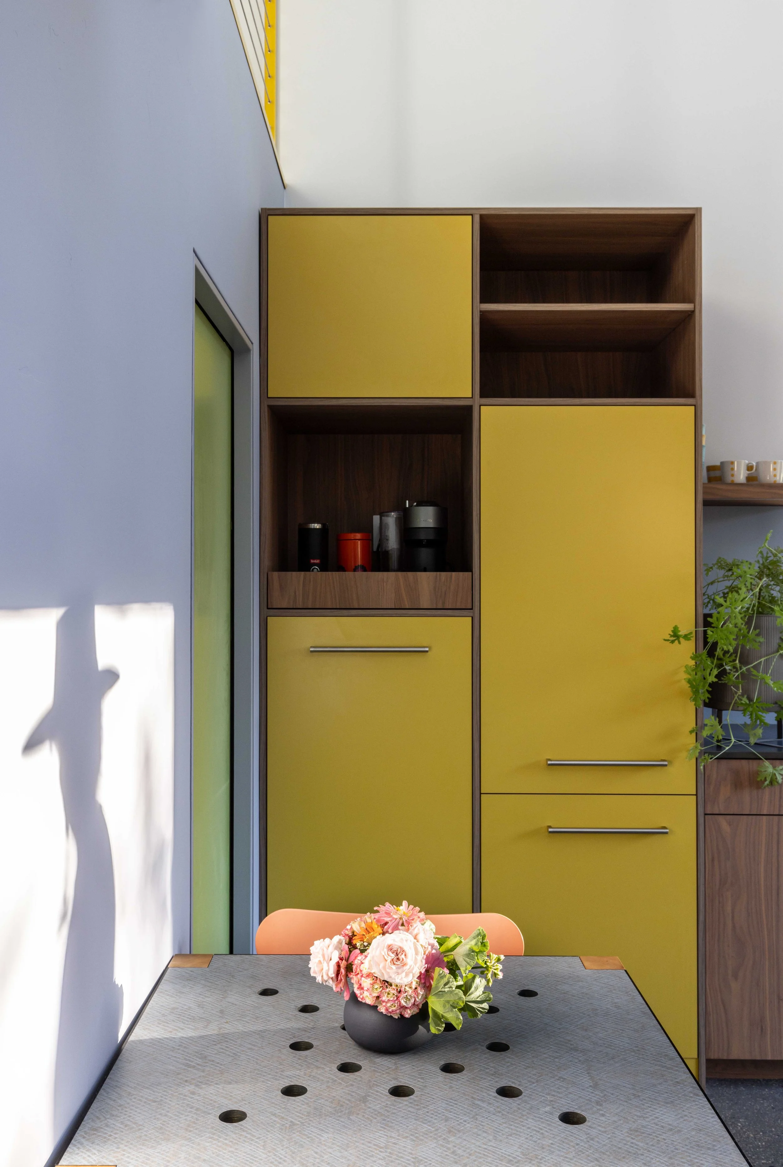 Kitchen with yellow cabinets, a modern table with circular cutouts, and a floral arrangement in a black vase.