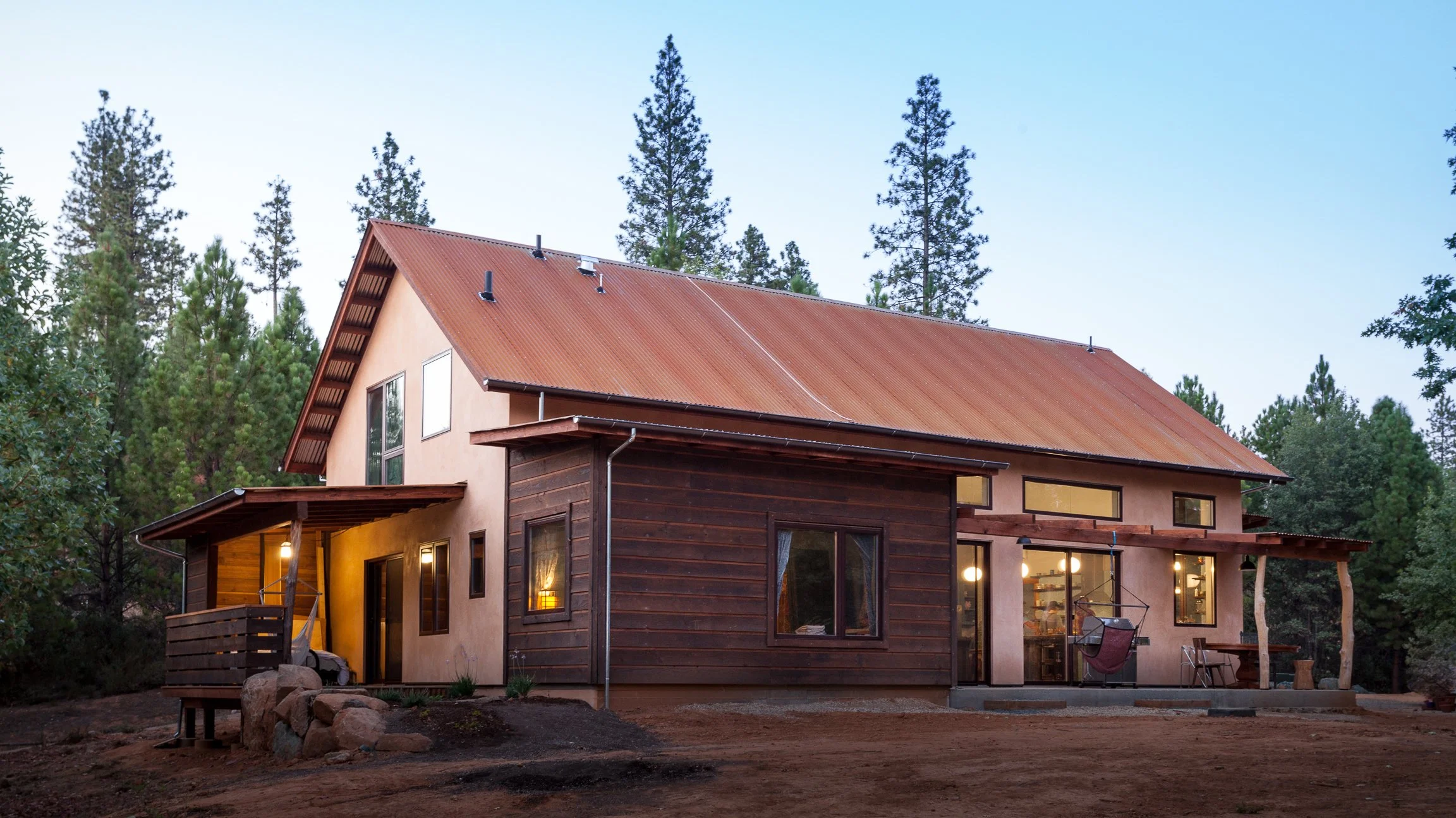Rustic house with wooden siding and metal roof surrounded by pine trees.