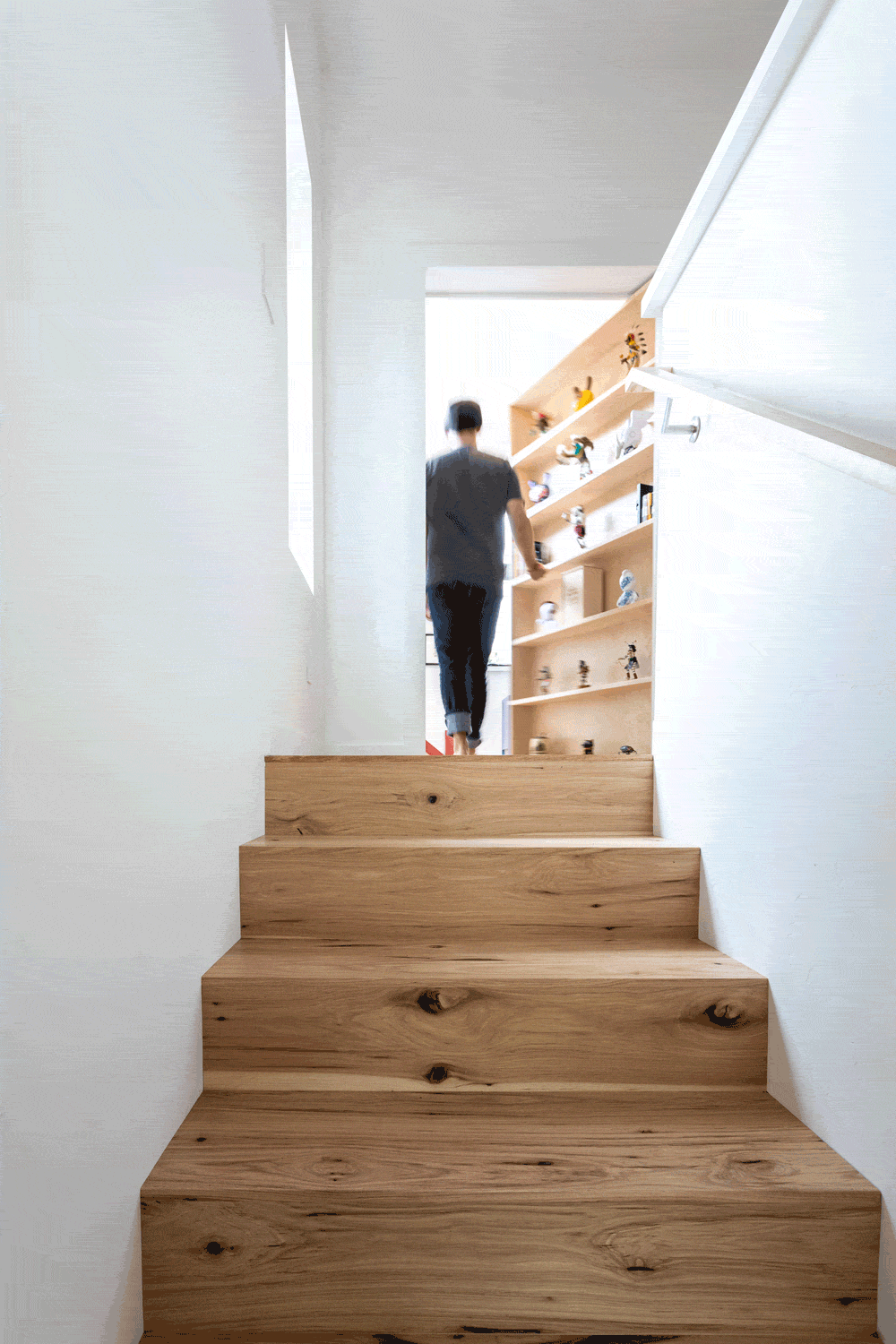 Person ascending wooden stairs towards a room with shelves full of figurines.
