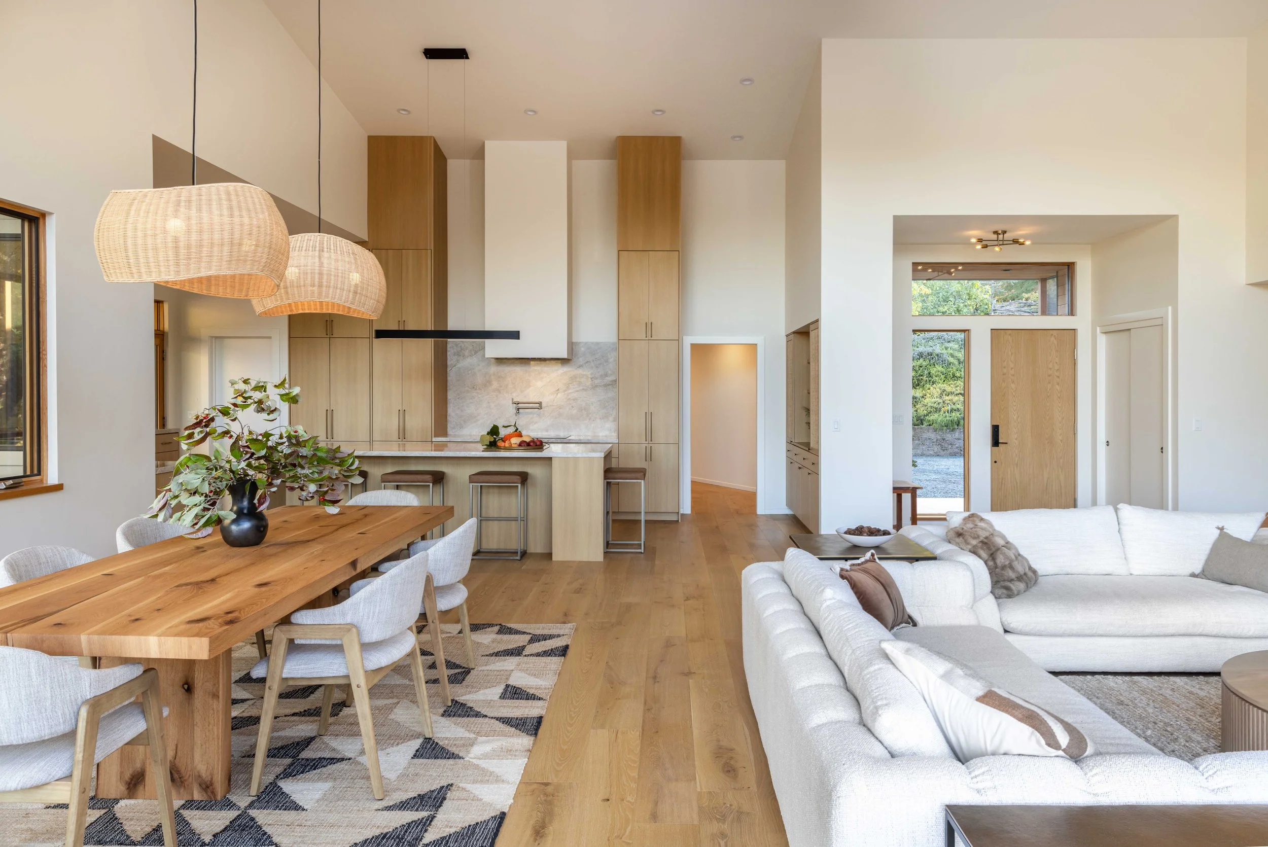 Modern open-plan kitchen and living room with wooden floors, dining table, pendant lighting, and white sofas.