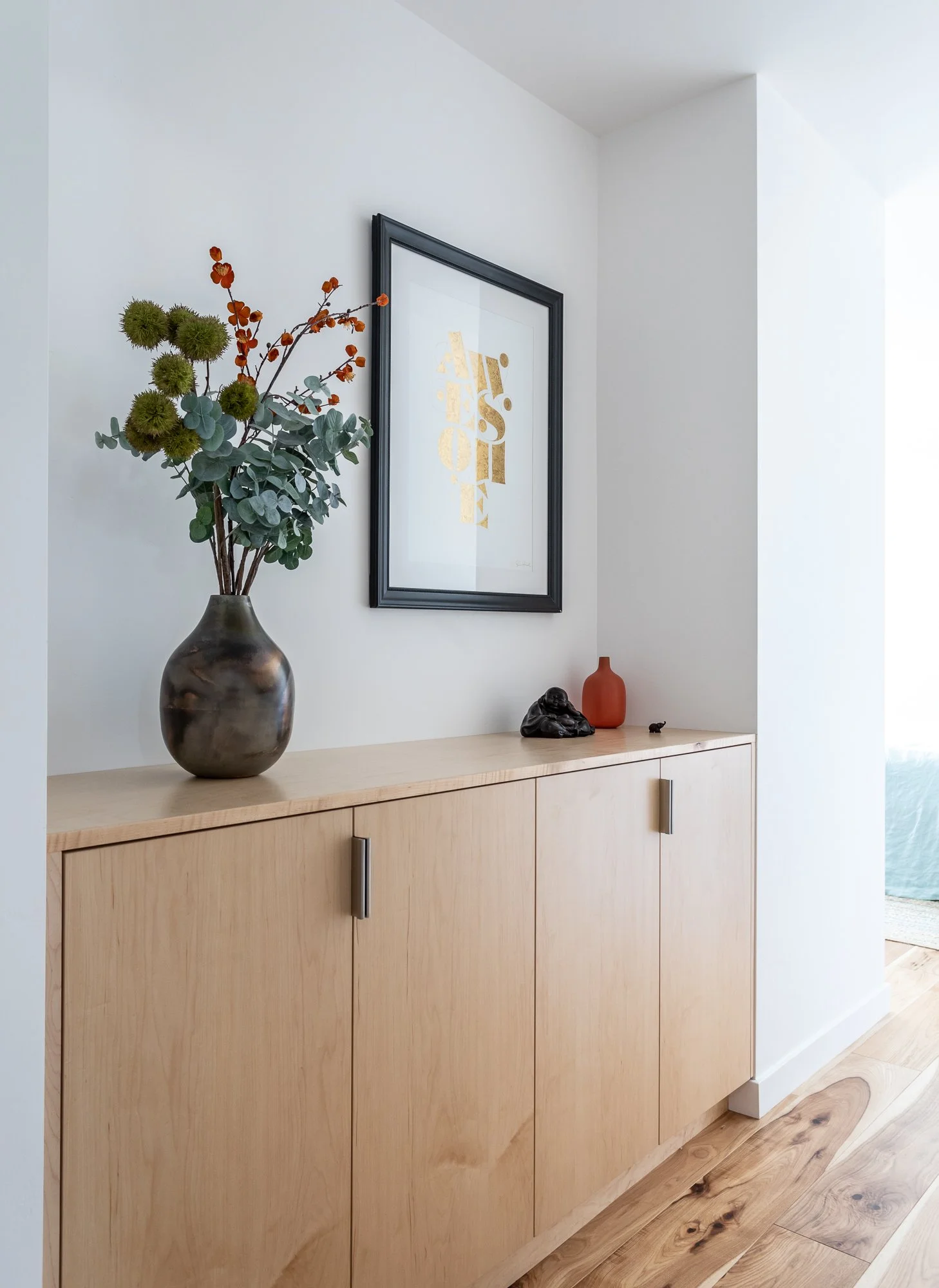 Modern interior with wooden cabinet, vase with foliage, framed artwork, and decorative objects.