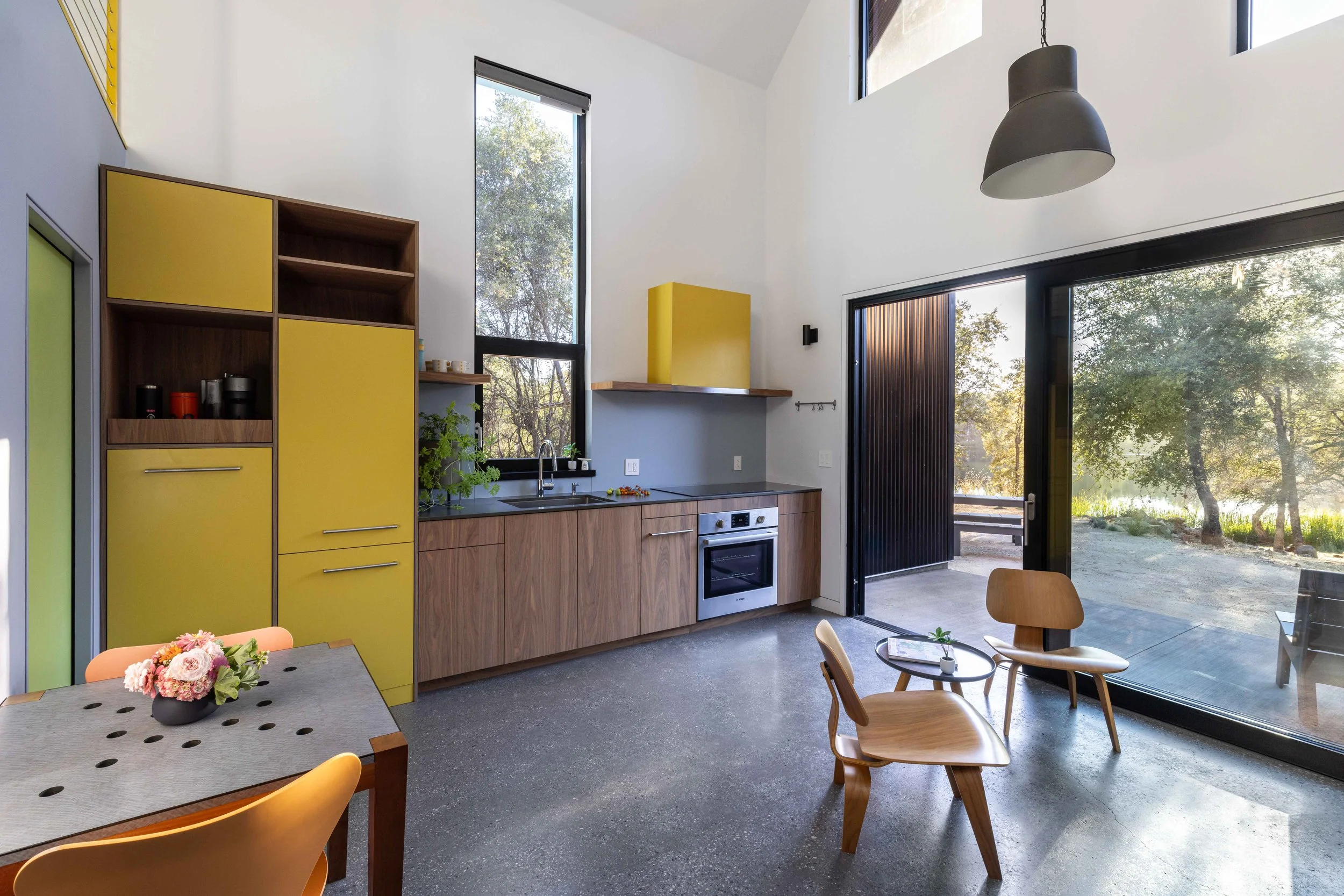 Modern kitchen with yellow cabinets and glass door overlooking outdoor scenery with trees.