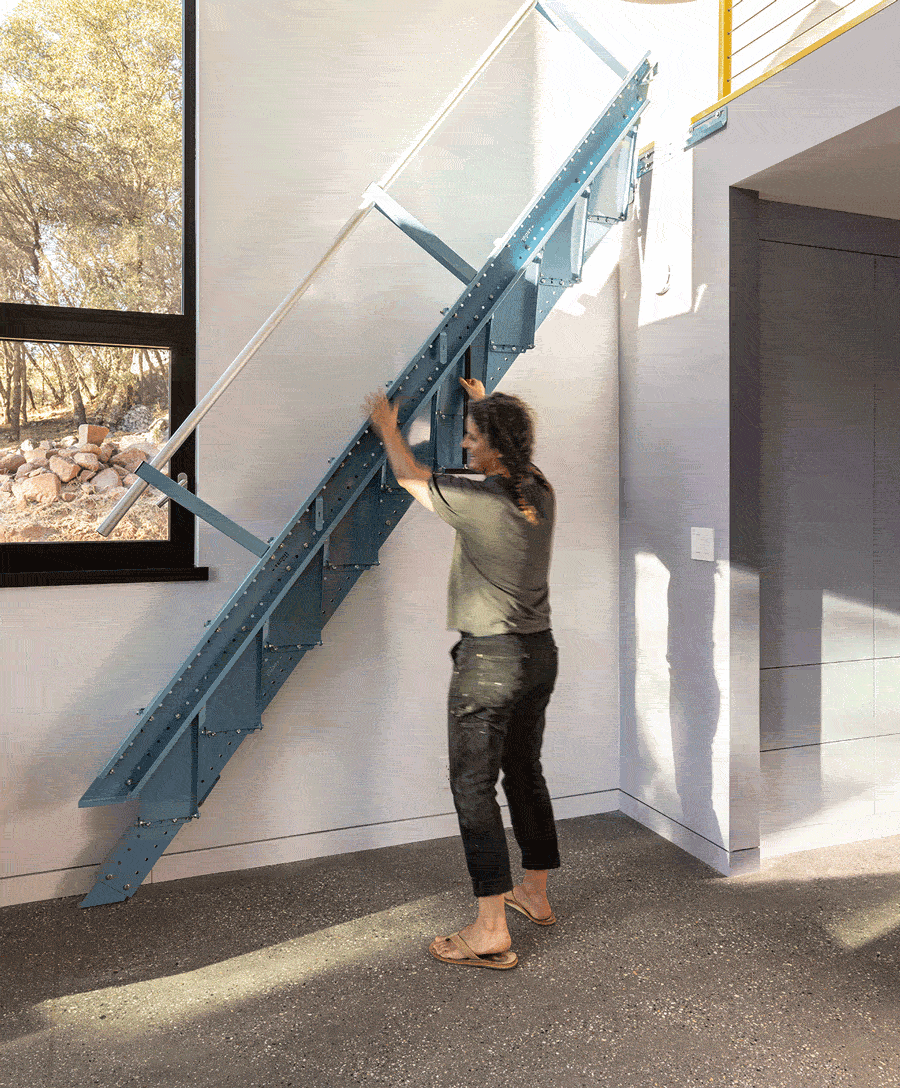 Person folding a retractable blue staircase against a wall in a modern interior space.