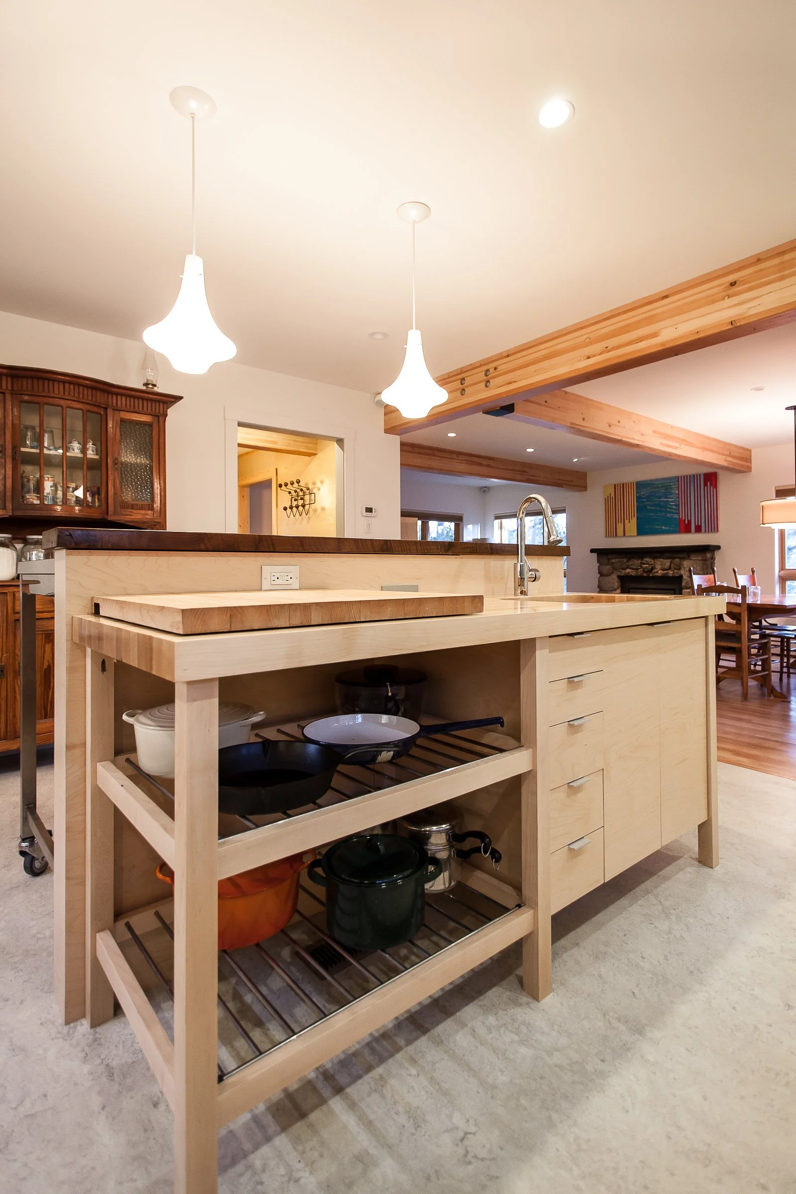 Modern kitchen interior with a wooden island featuring a cutting board, open shelves with pots, pendant lights, and surrounding cabinetry.