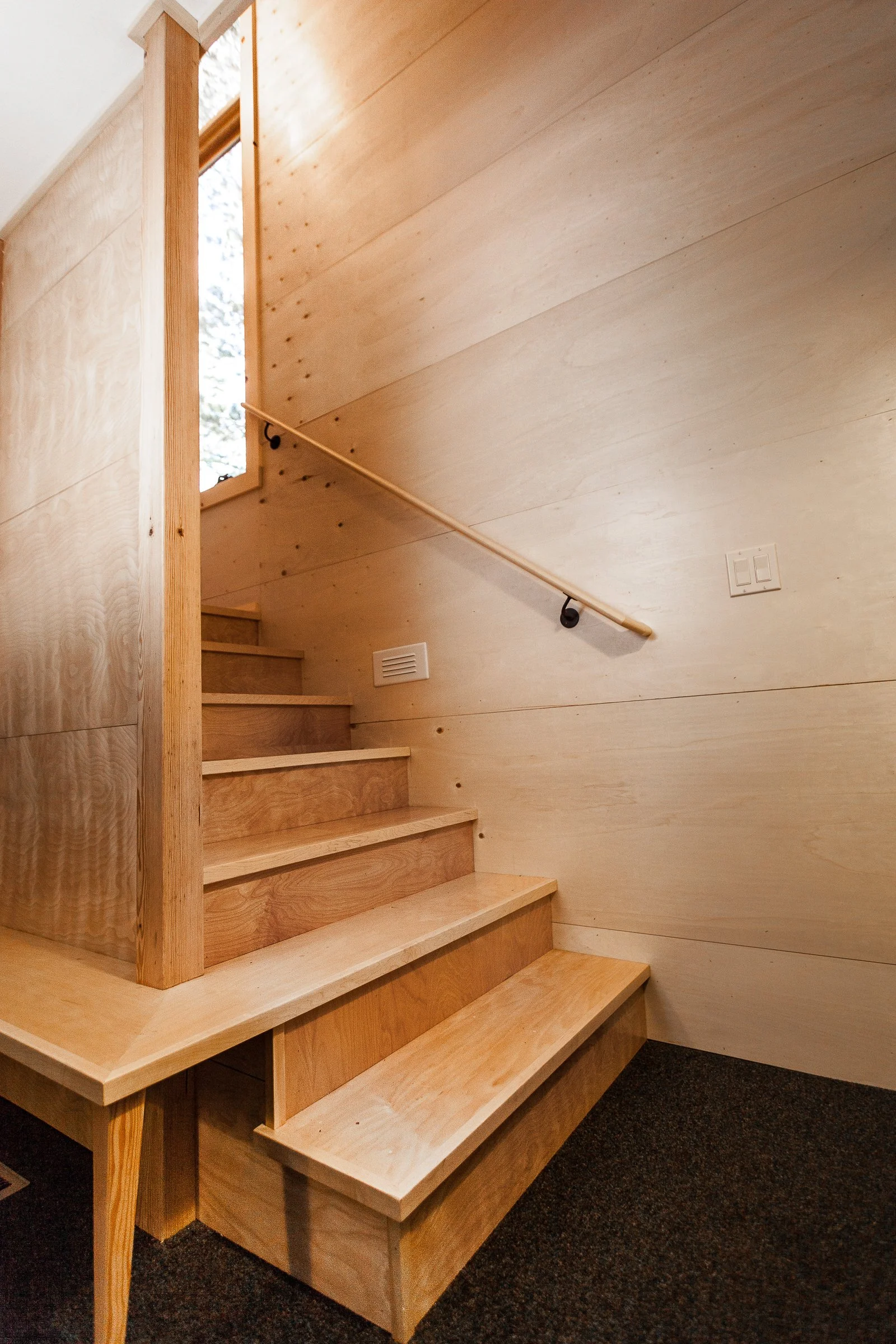Wooden staircase with handrail and light wood paneling in a modern interior space.