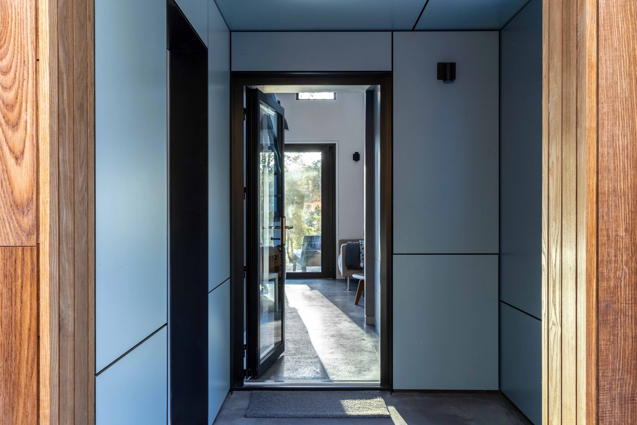 Modern hallway with wooden paneling and open glass door leading to bright living area
