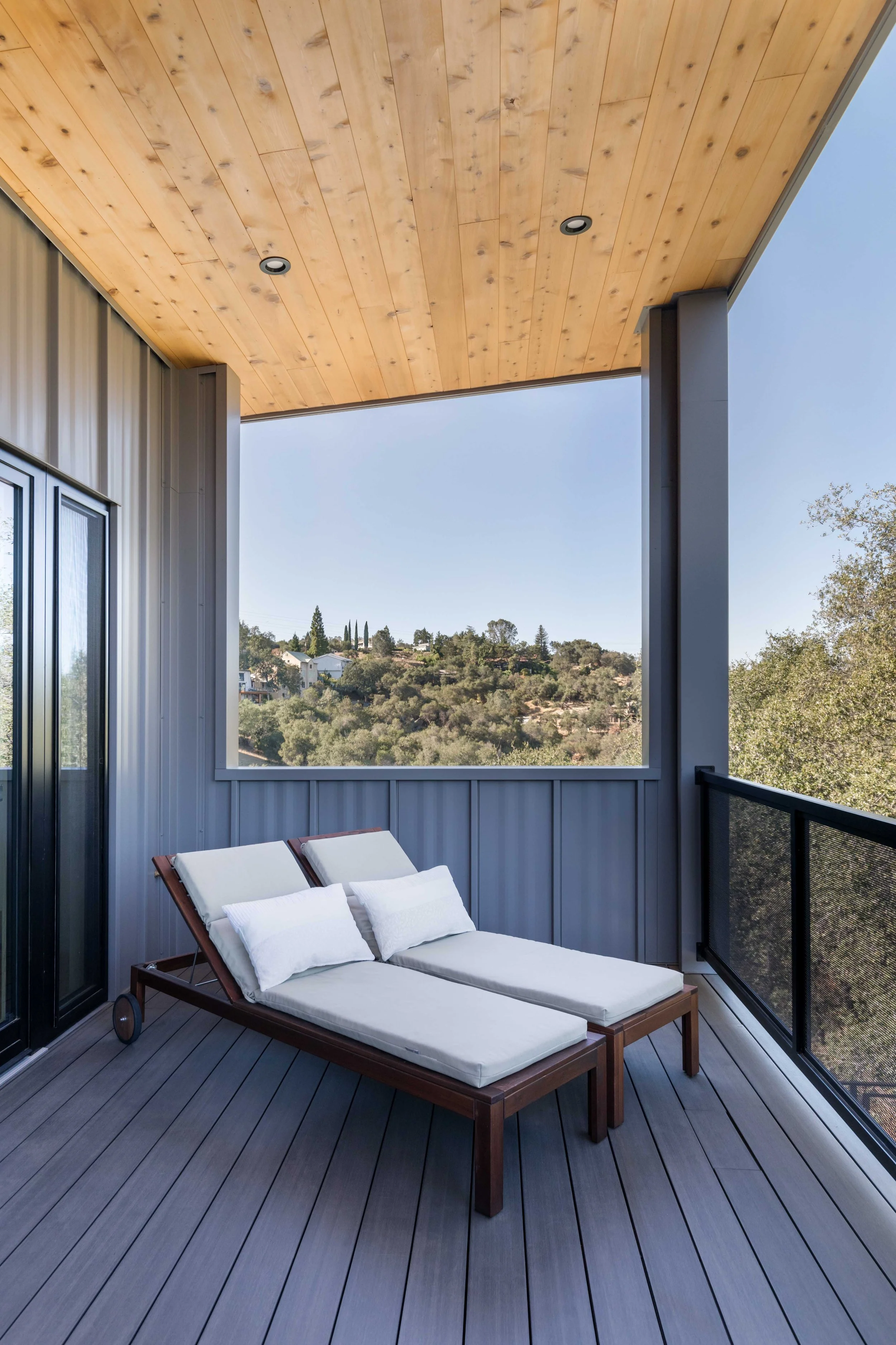 Modern balcony with wooden lounge chairs and view of trees and hills.