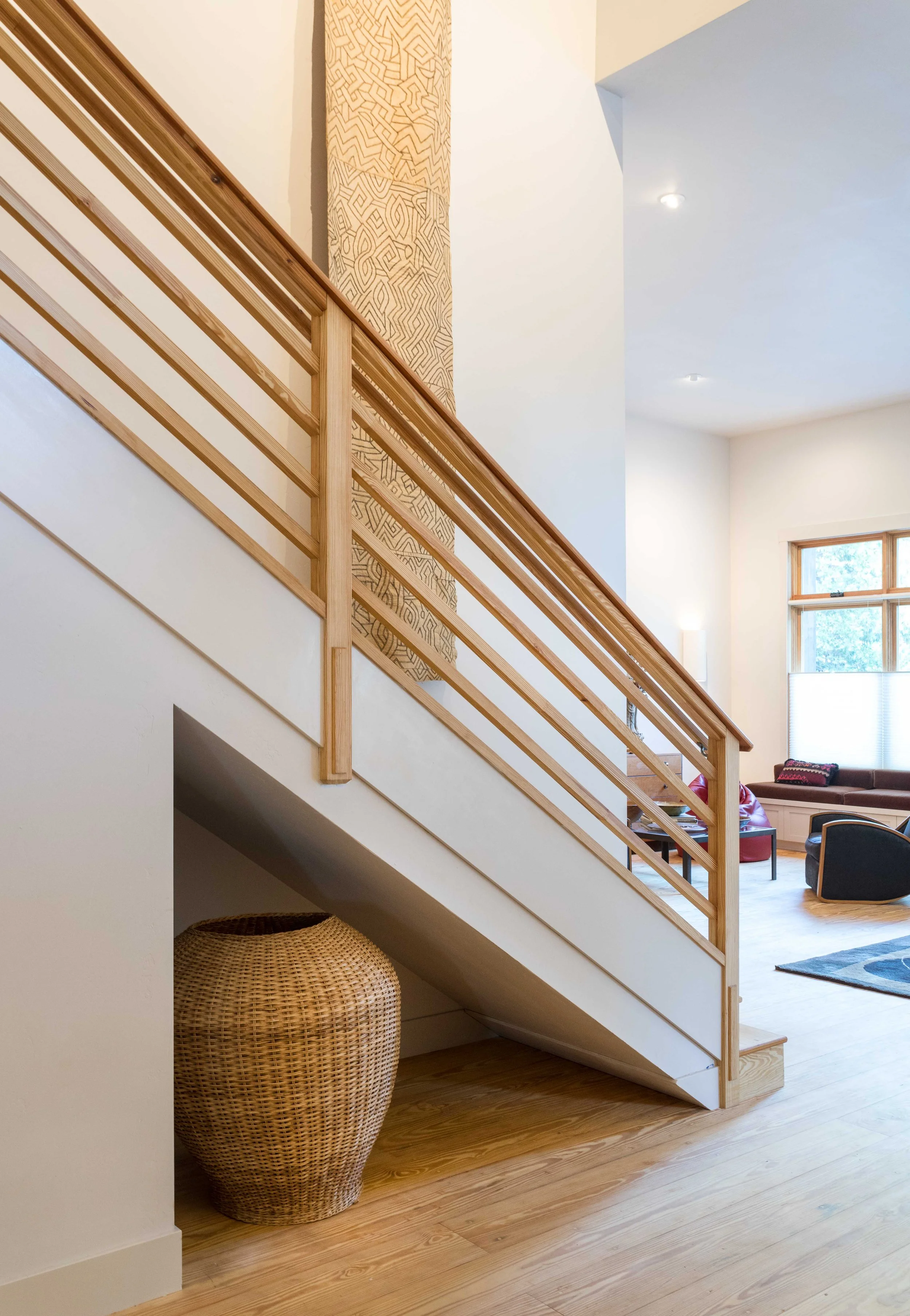 Modern interior with a wooden staircase, wicker basket, patterned wall hanging, and scenic window view.