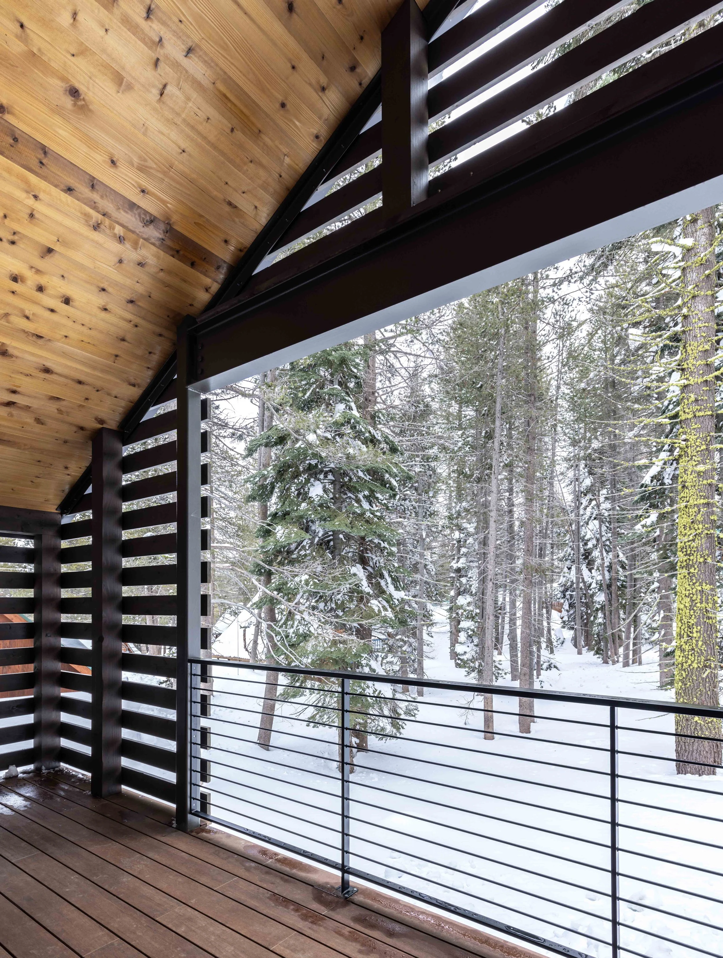 Modern wooden porch with slatted walls and snow-covered trees in the background.
