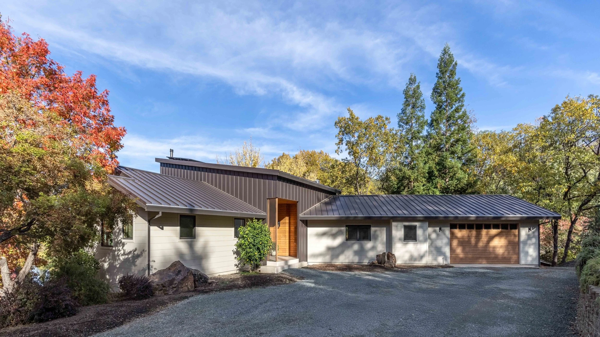 Modern single-story house with metal roof surrounded by autumn trees.