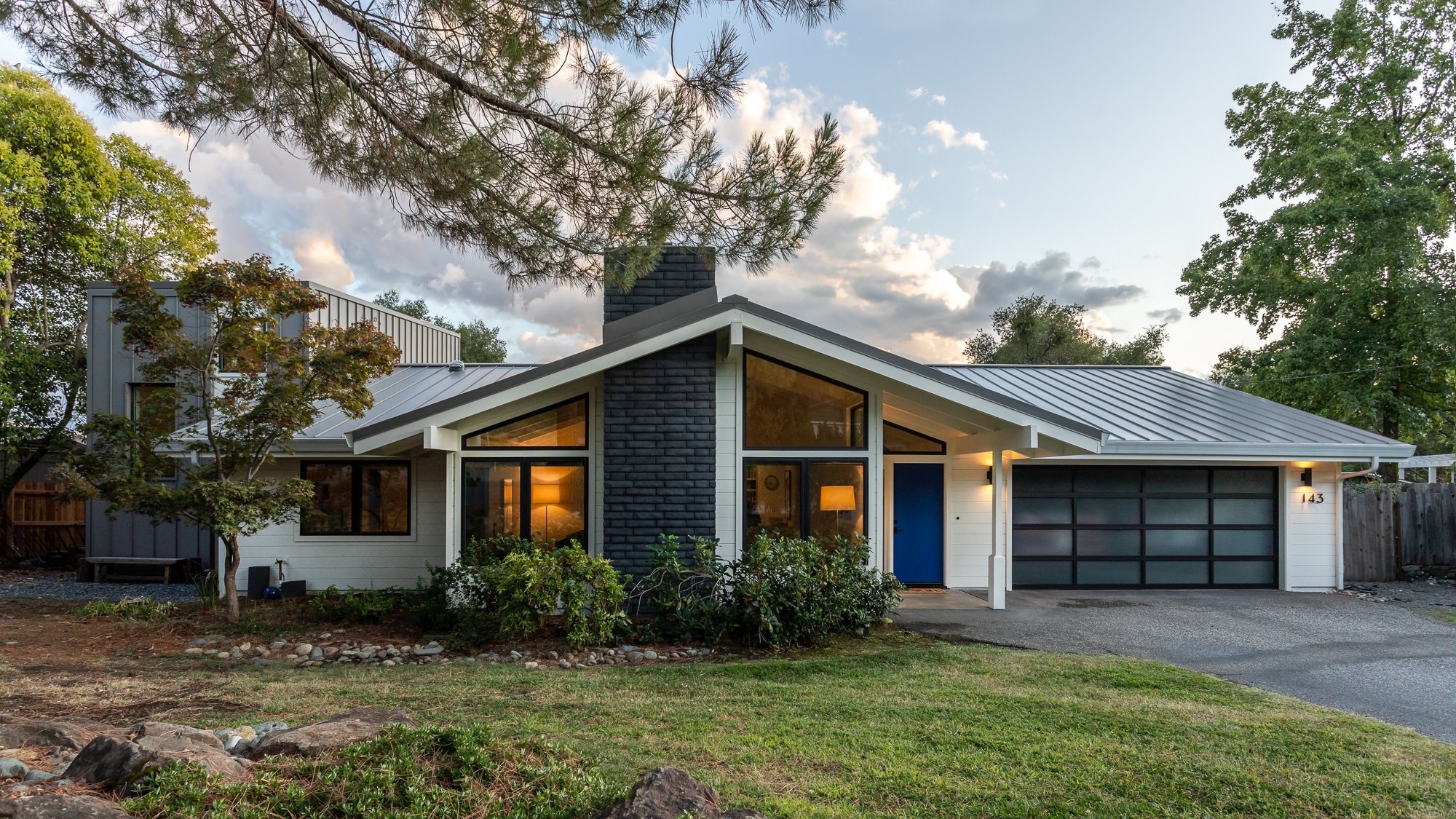 Modern ranch-style house with large windows, metal roof, and blue door.