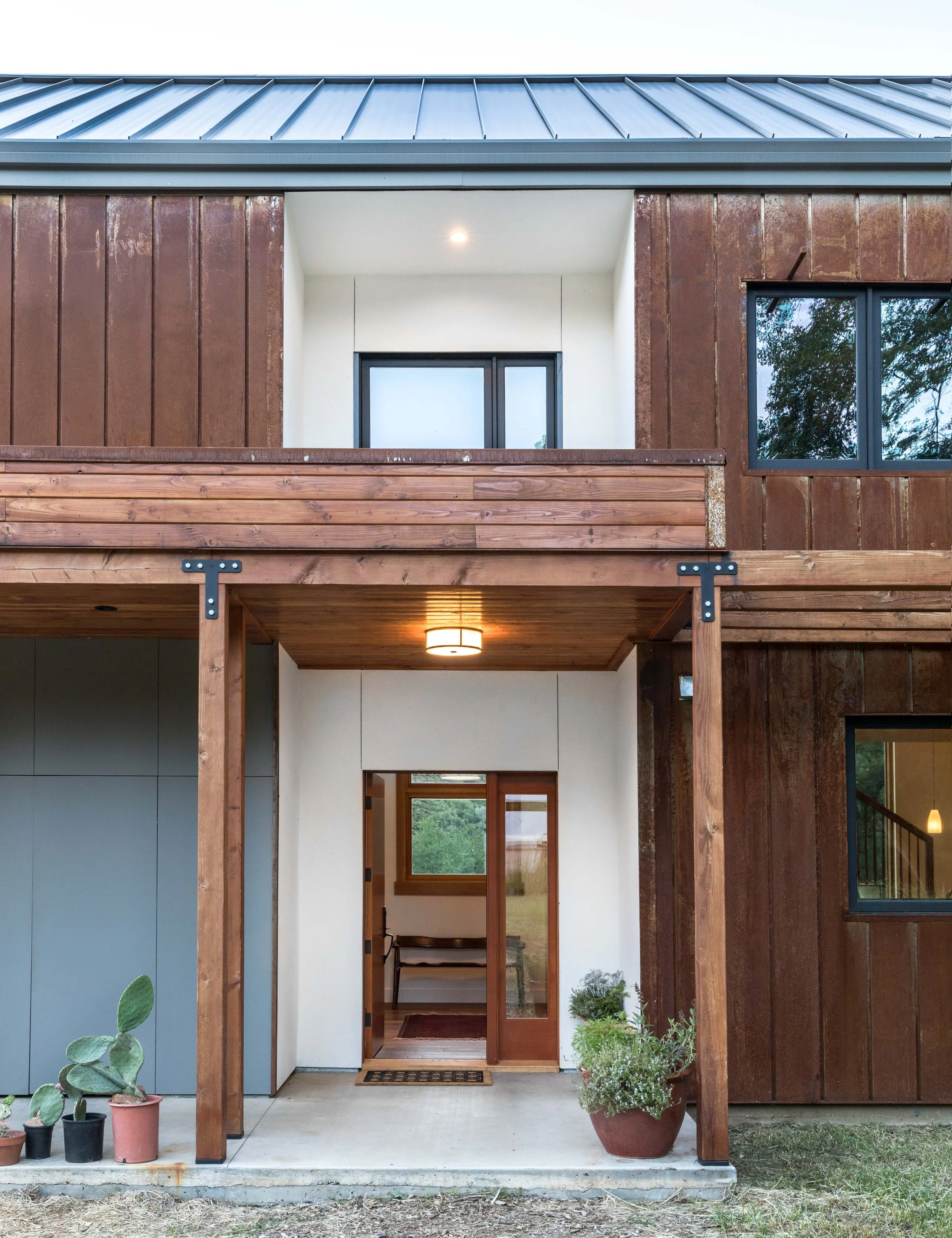 Modern house entry with wood and metal elements, featuring potted plants by the entrance and a covered doorway.