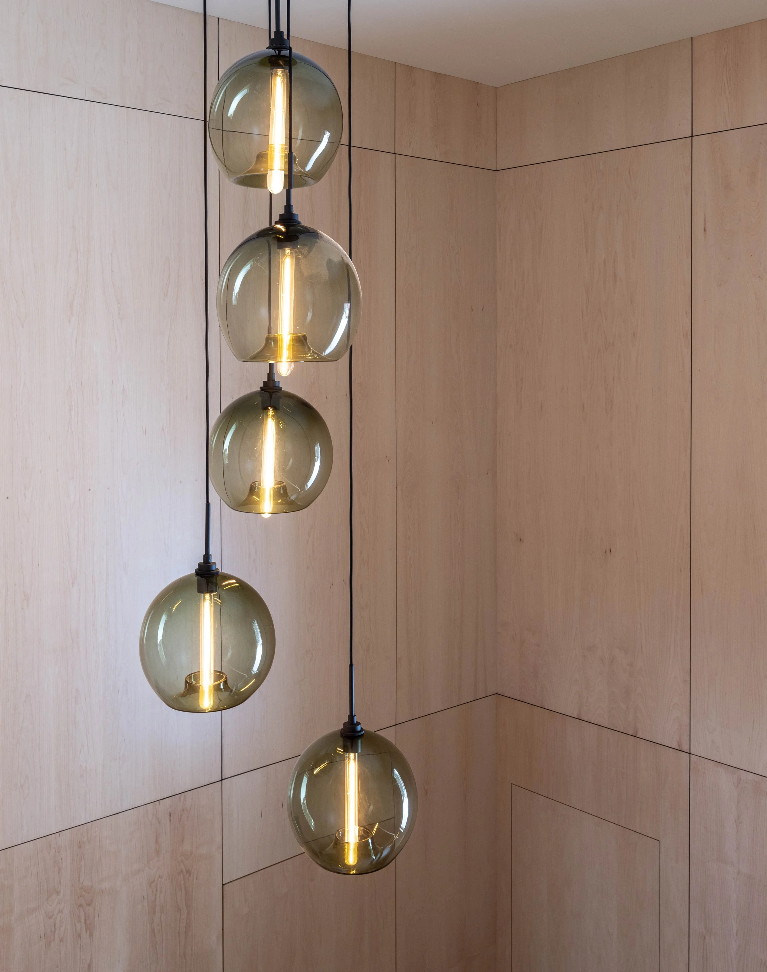 Modern spherical pendant lights hanging in front of wooden paneled wall.