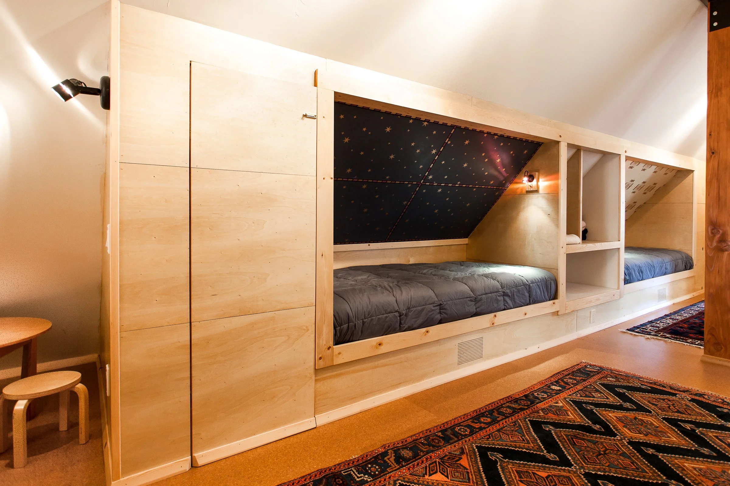 Minimalist bedroom with built-in bunk beds and light wood paneling, featuring a star-patterned ceiling and modern lighting.