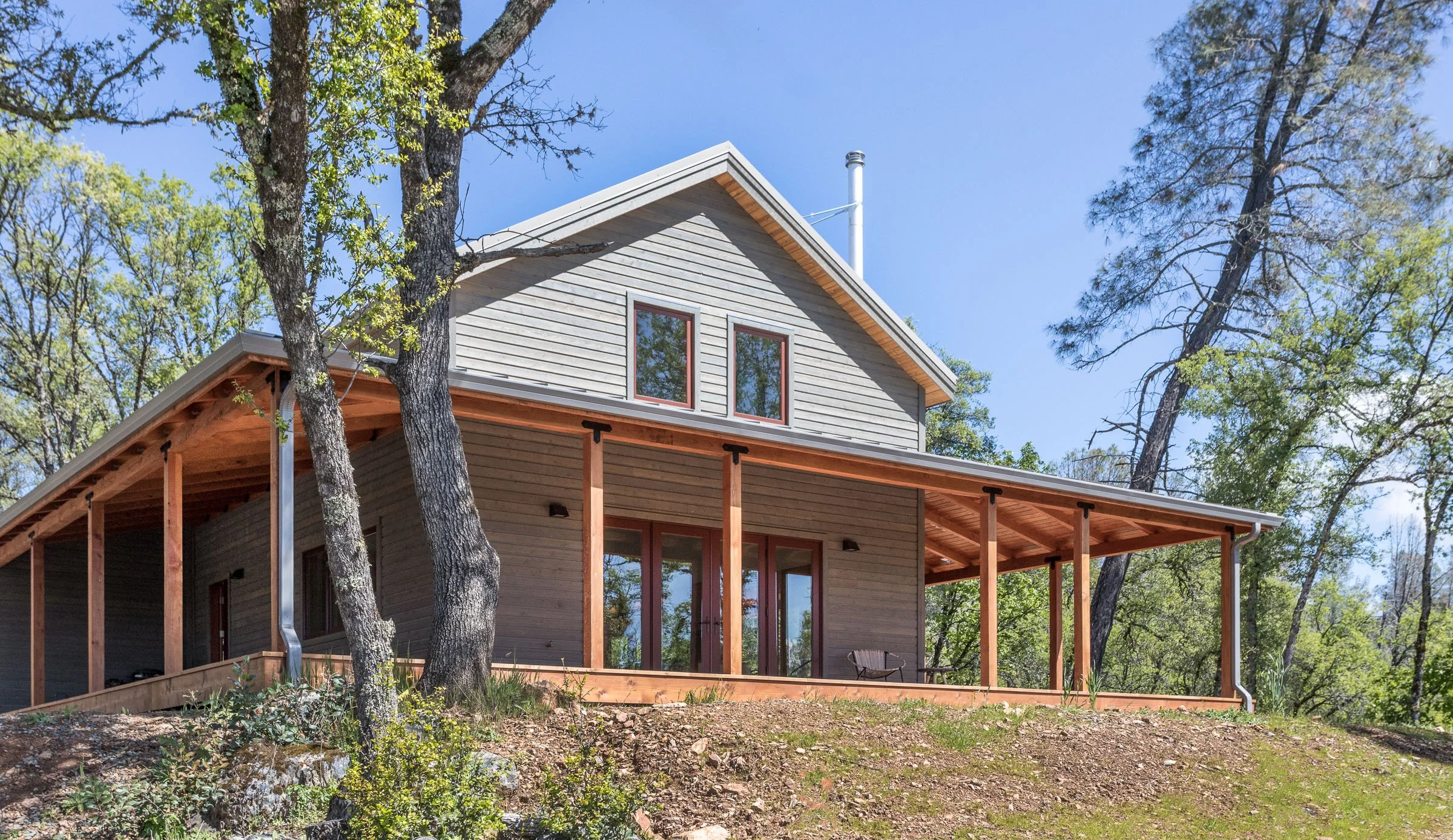 A modern cabin with wood siding and a covered porch, surrounded by trees.