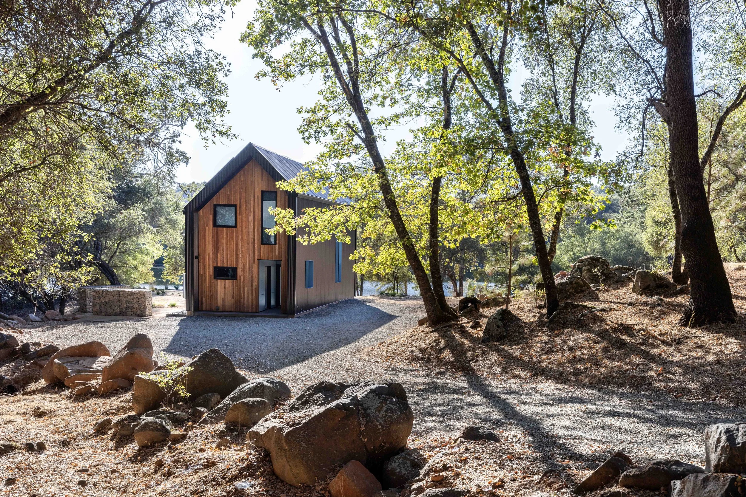 A high-performance home by Atmosphere Design Build nestled among oak trees and granite boulders in the Northern California Sierra foothills, featuring cedar siding and a standing seam metal roof.