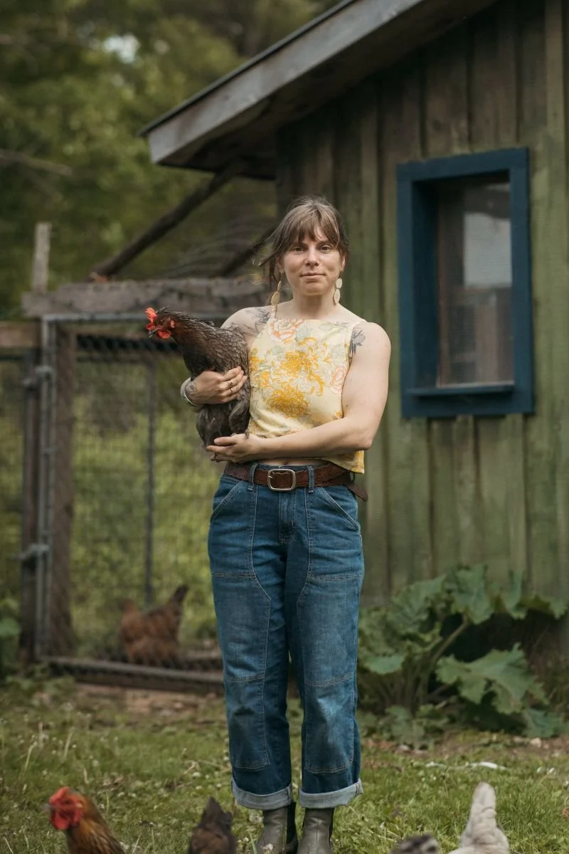  Abby stands in front of a chicken coop with their hen Silverwing in their arms. Abby has ash blonde hair, a pale complexion, and a super cute outfit on. Photo courtesy of Sunbird Photography. 