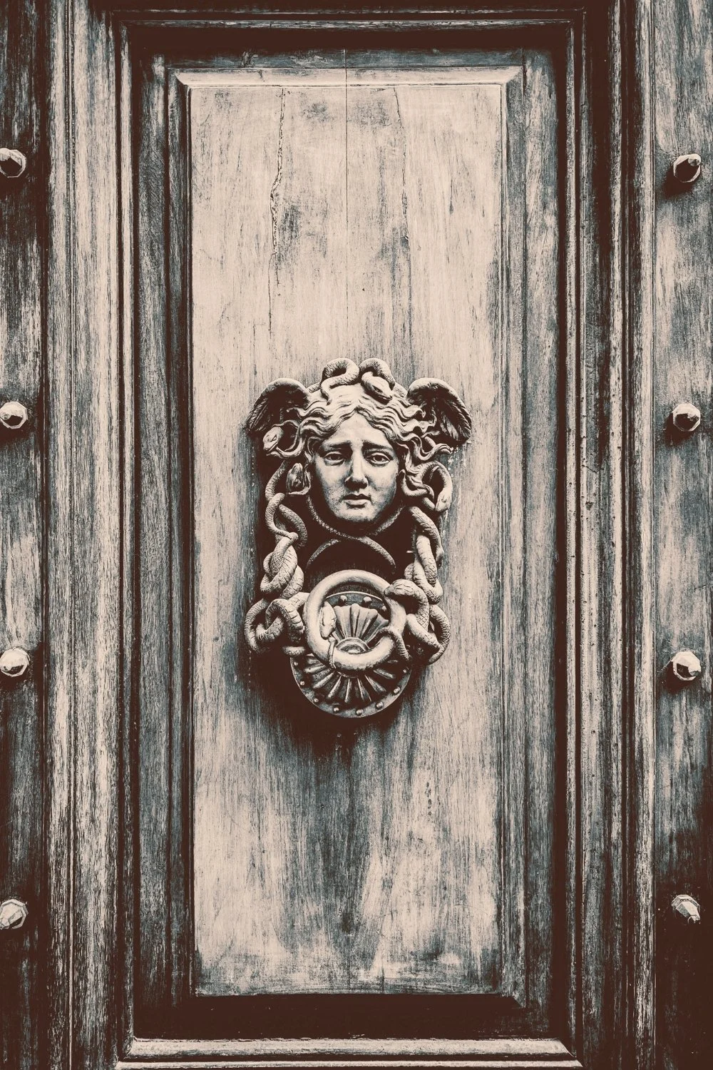 Medusa-themed door knocker on aged wooden door for scented handmade mythology candles with wooden wicks.