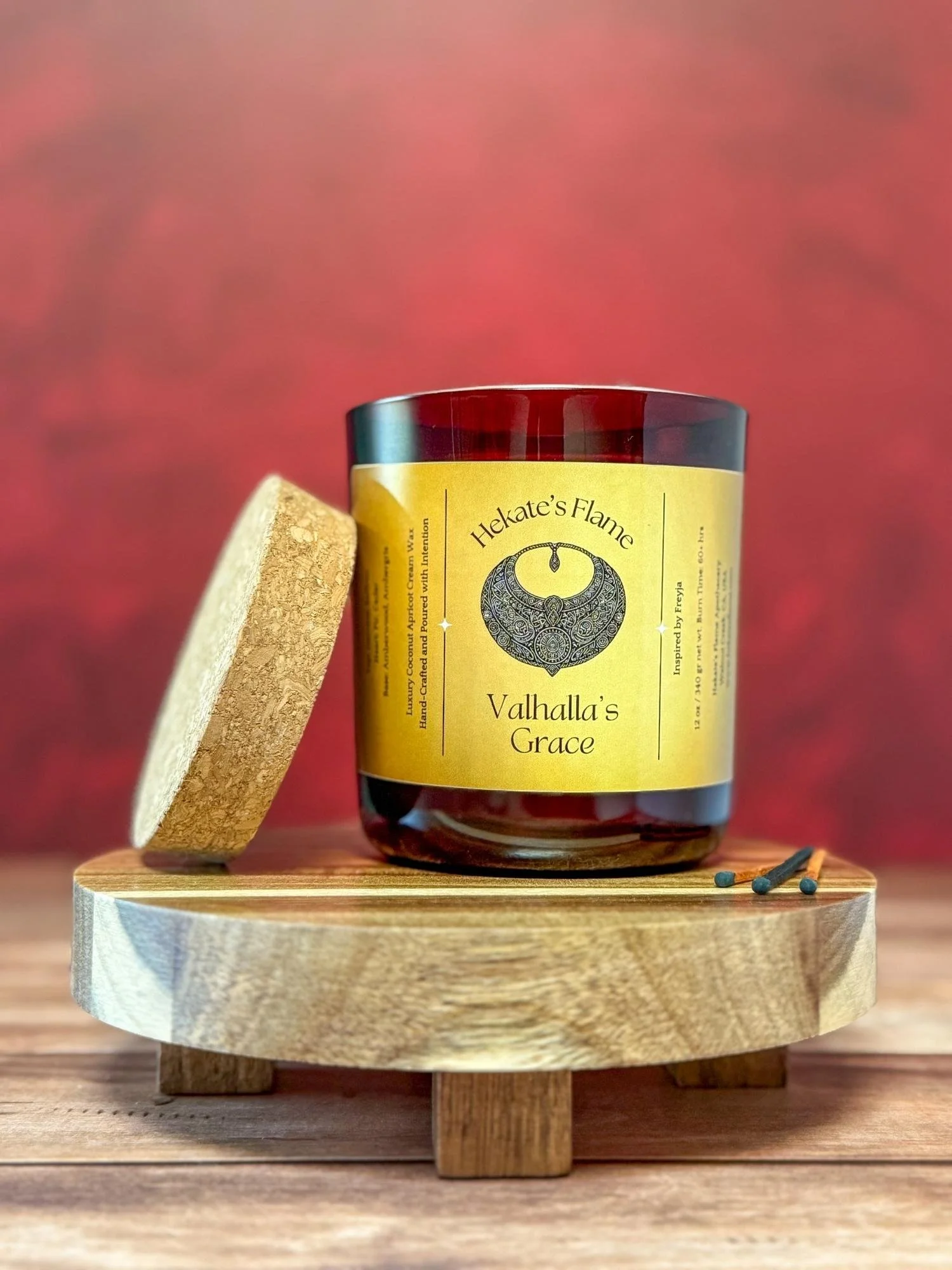 Helheim’s Mist Norse mythology candle in a wine red translucent glass jar with cork lid, hand-poured coconut apricot wax with a wooden wick, eco-conscious artisan design.
