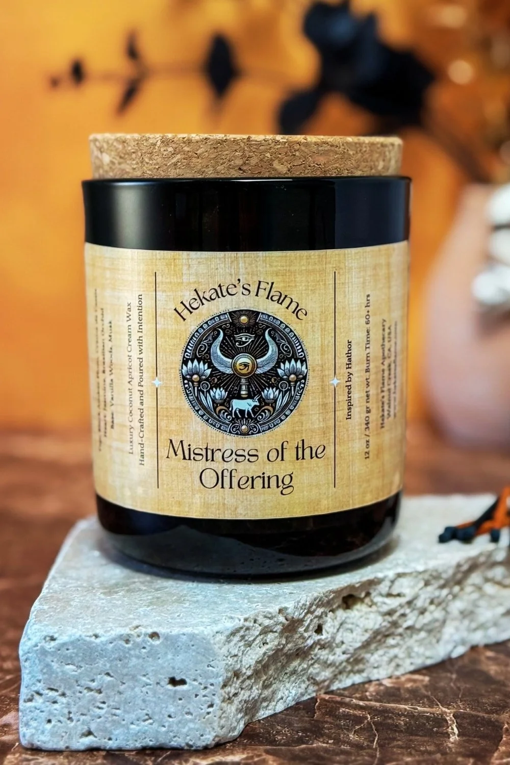 Handmade Egyptian goddess candle honoring Hathor, poured in a translucent smoky glass jar with coconut apricot wax and a wooden wick.