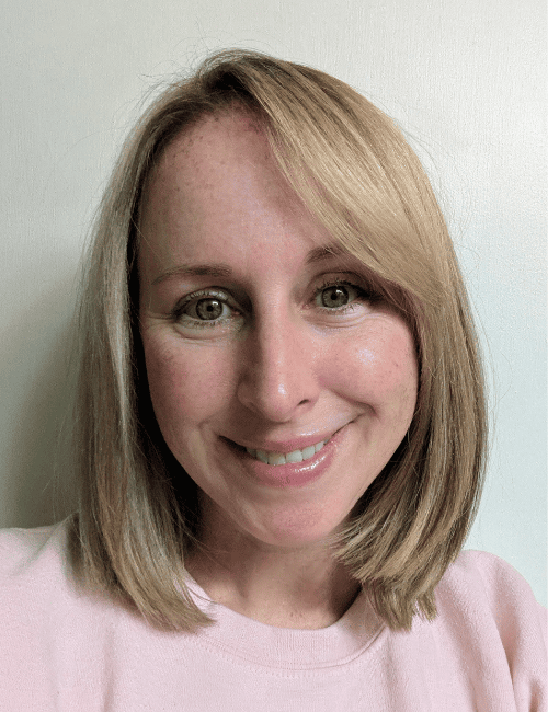 Woman smiling with medium length hair wearing a pink shirt.