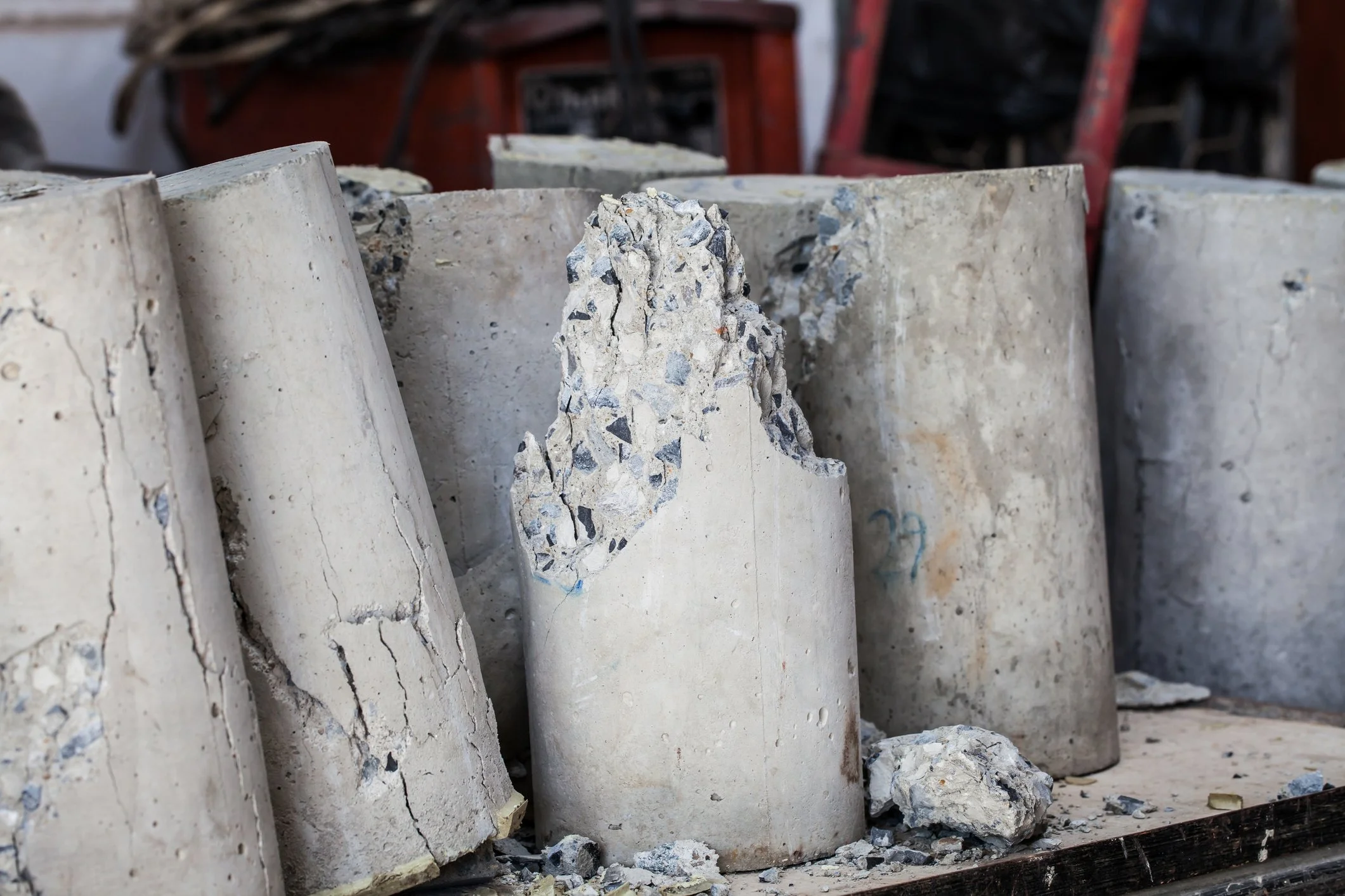 Cut sections of concrete pipes, with some damaged and cracked, placed outdoors on a wooden surface.