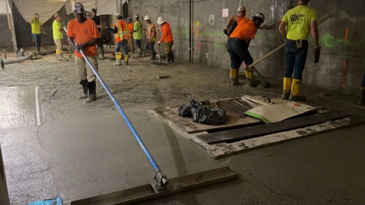 Construction workers spread wet concrete on a floor at a construction site.