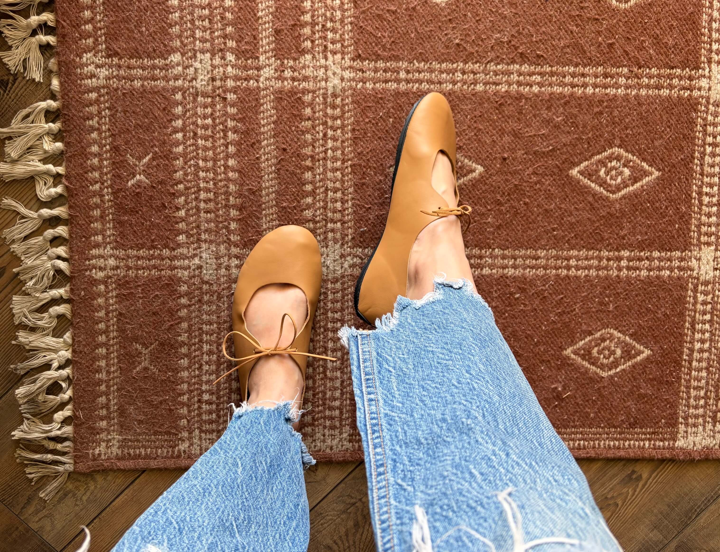 woman standing on a rug pointing one foot while wearing softstar shoes barefoot vintage tie ballerine flats