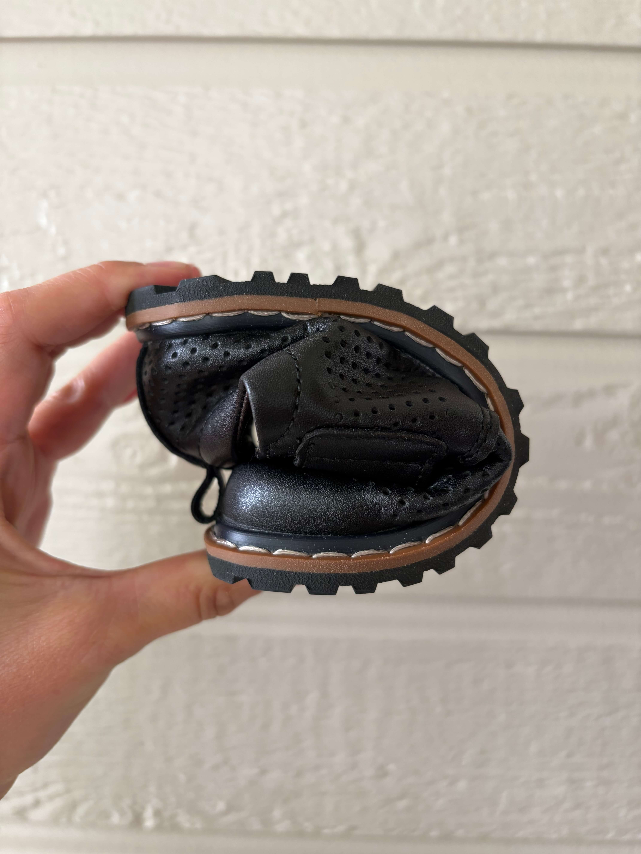 woman holding a pair of the Saguaro Kid's Form I Air Perforated Leather Barefoot Shoes and folding it in half to show its flexibility