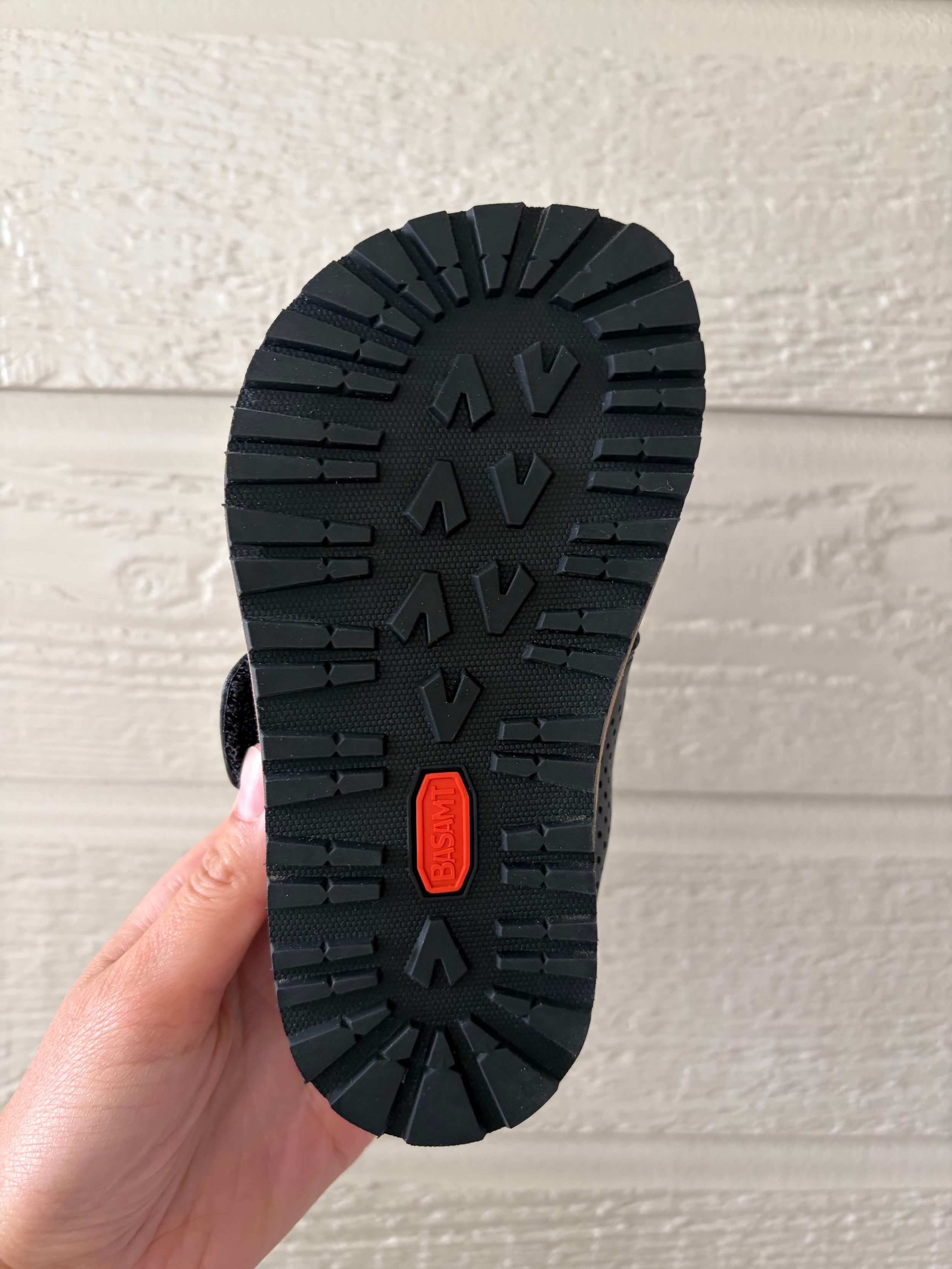 woman holding a pair of the Saguaro Kid's Form I Air Perforated Leather Barefoot Shoes and showing the sole and its wide and natural foot shaped design