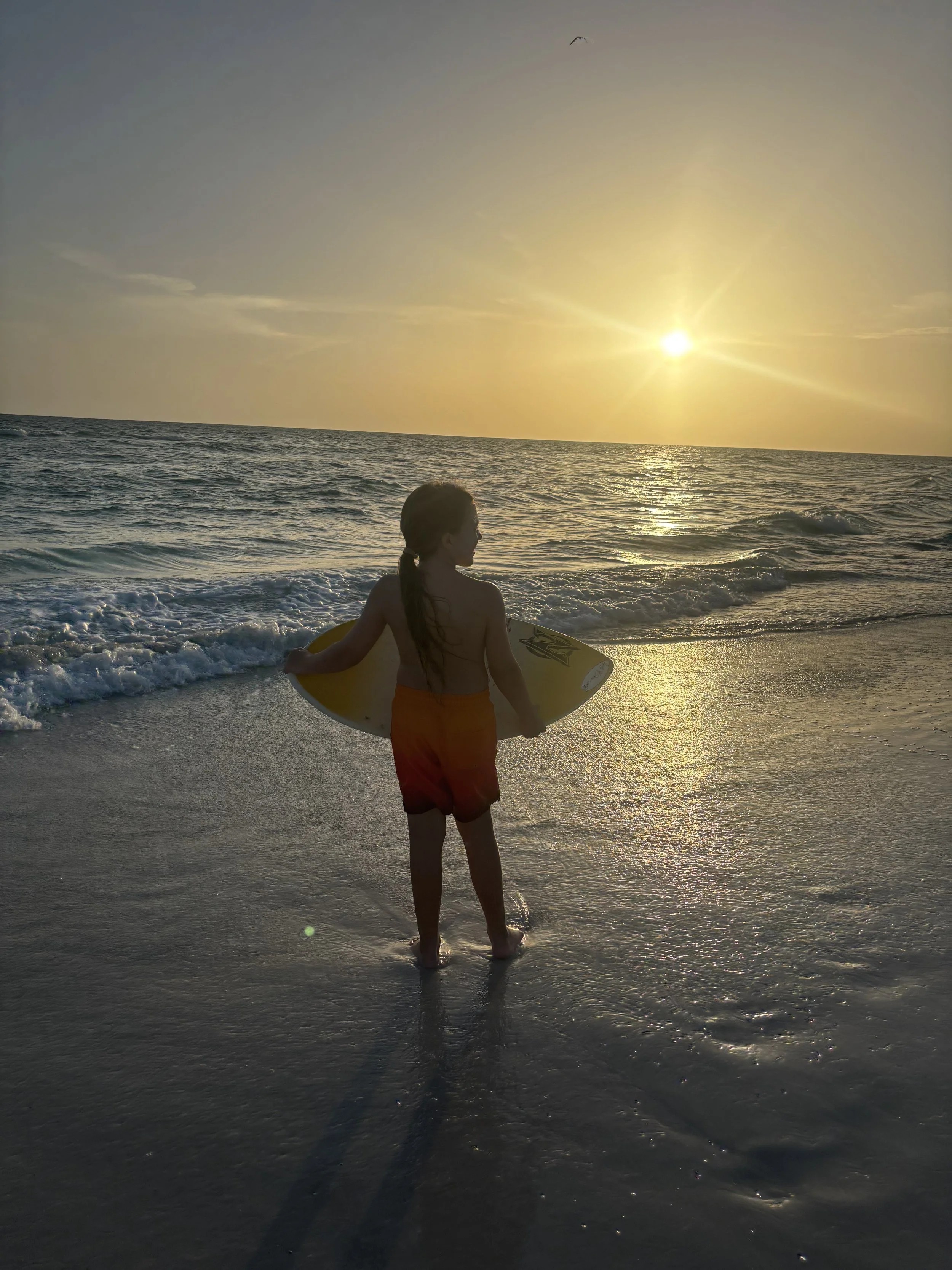 Skimboarder carrying a board on Anna Maria Island at sunset with AMI Skim and Surf.