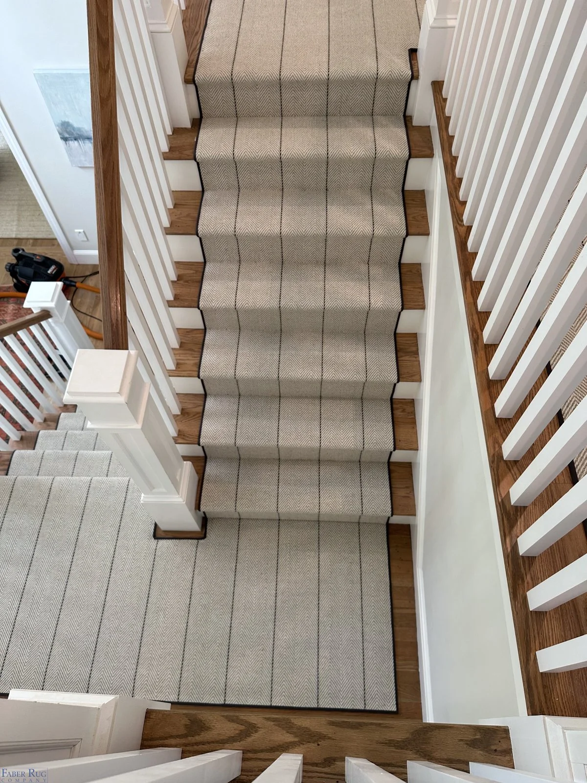 Overhead view of staircase with beige and black patterned runner, wooden steps, white railings, and adjacent hardwood floor.