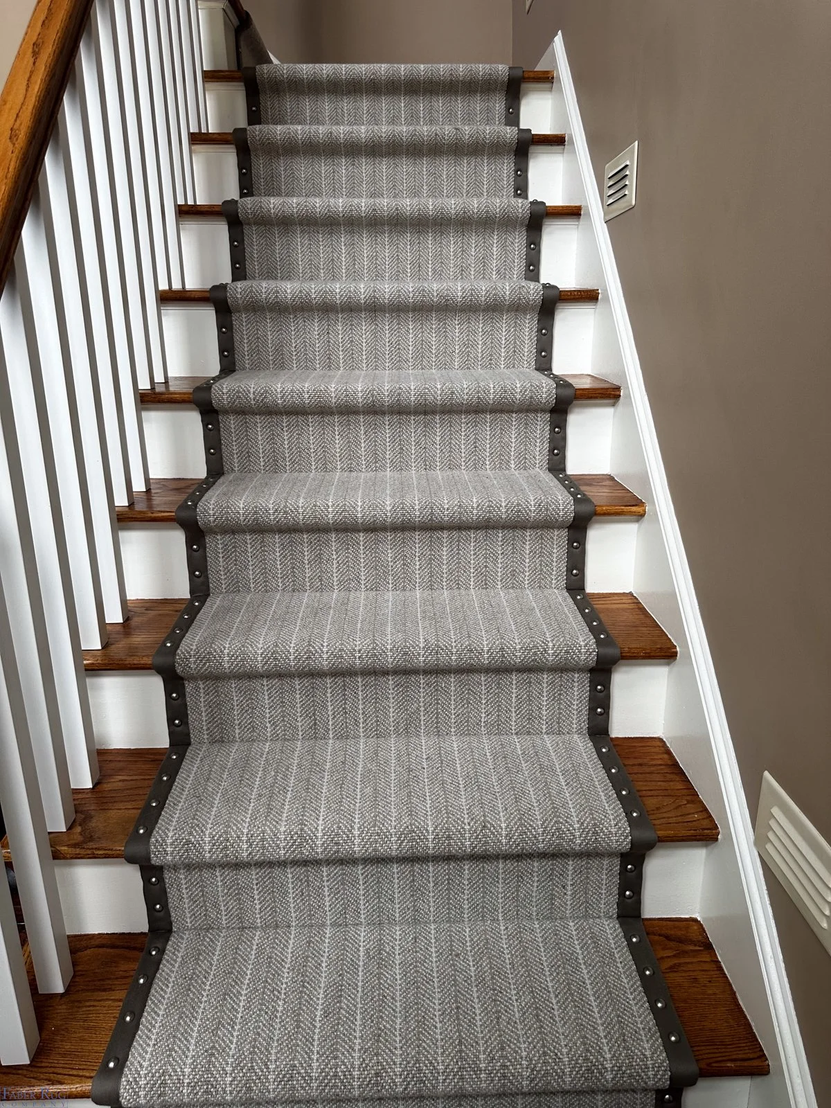 Carpeted staircase with wooden steps, white railings, and beige walls.