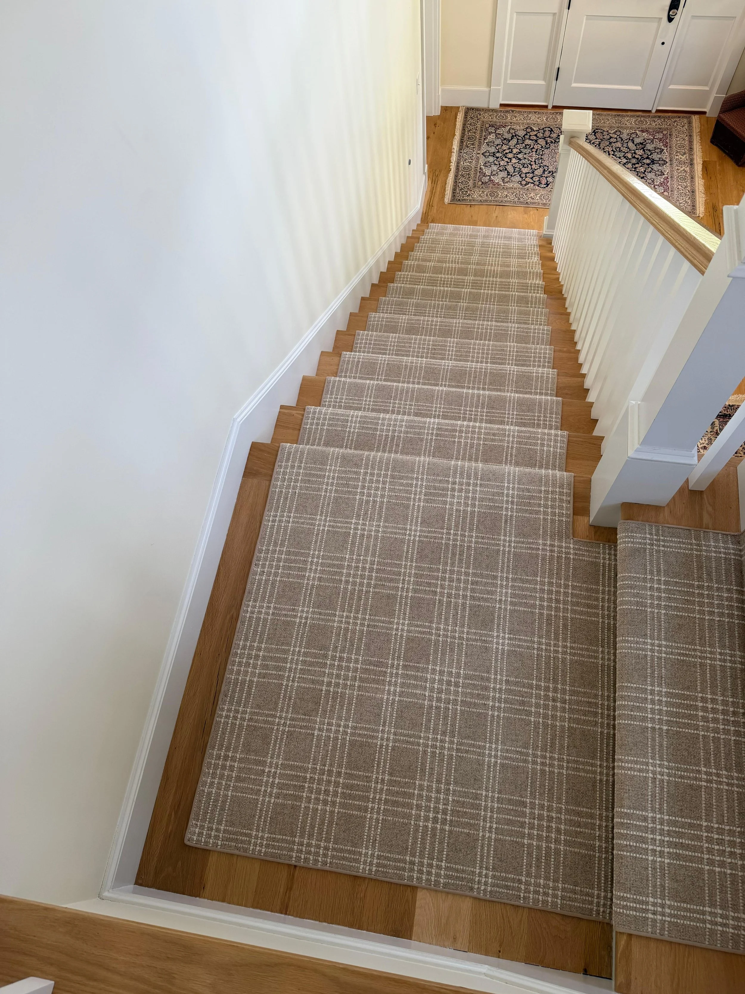 View of a staircase with beige patterned carpet and wooden stairs, leading down to a room with hardwood flooring, a patterned rug, and white doors.