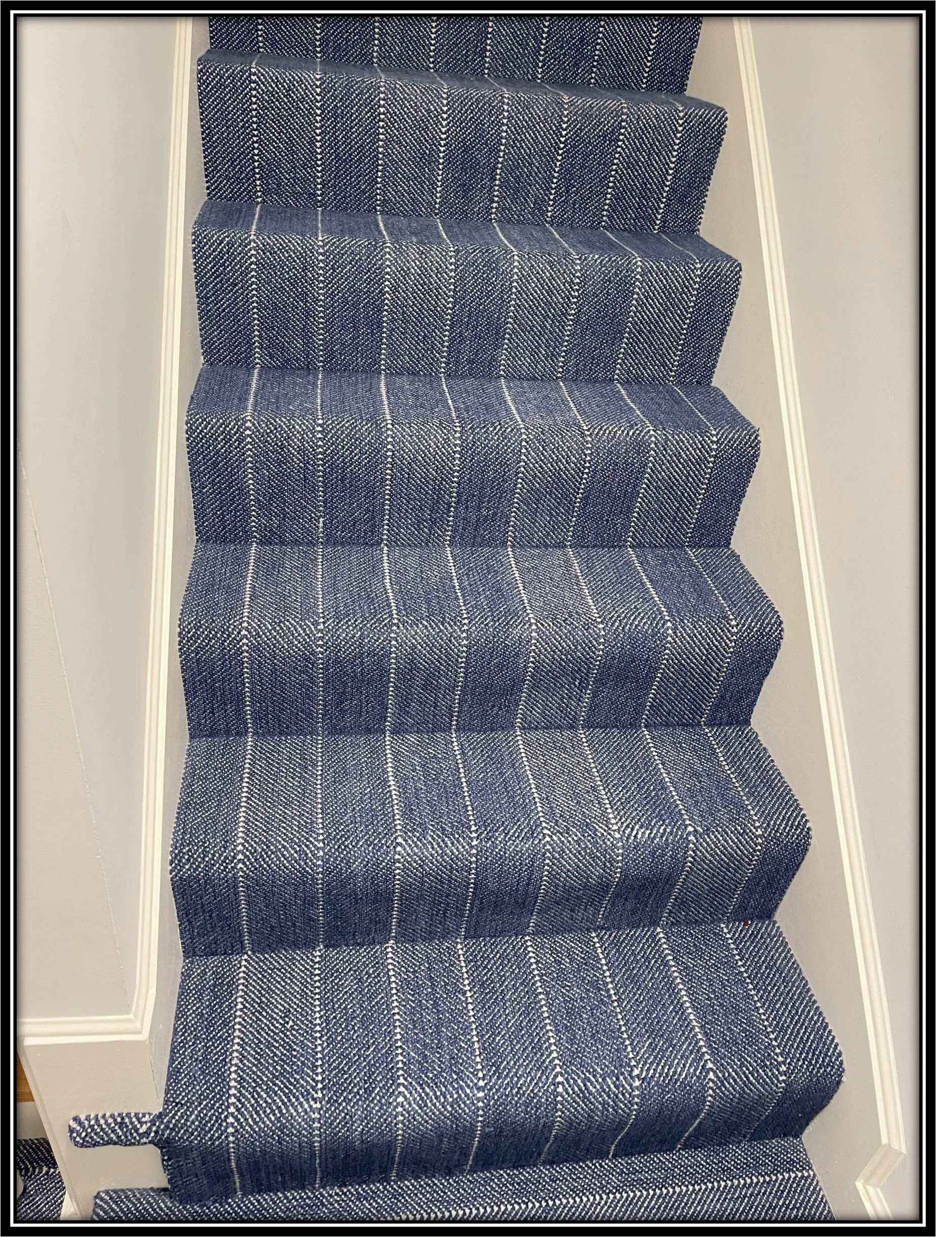 Carpeted staircase with a blue and white plaid pattern, bordered by white walls and white trim.