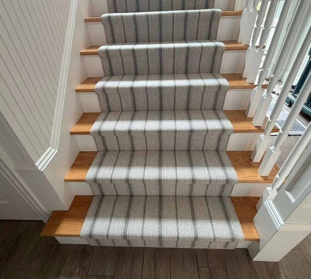 Wood staircase with beige and gray plaid carpet runner, white risers, and white spindles.
