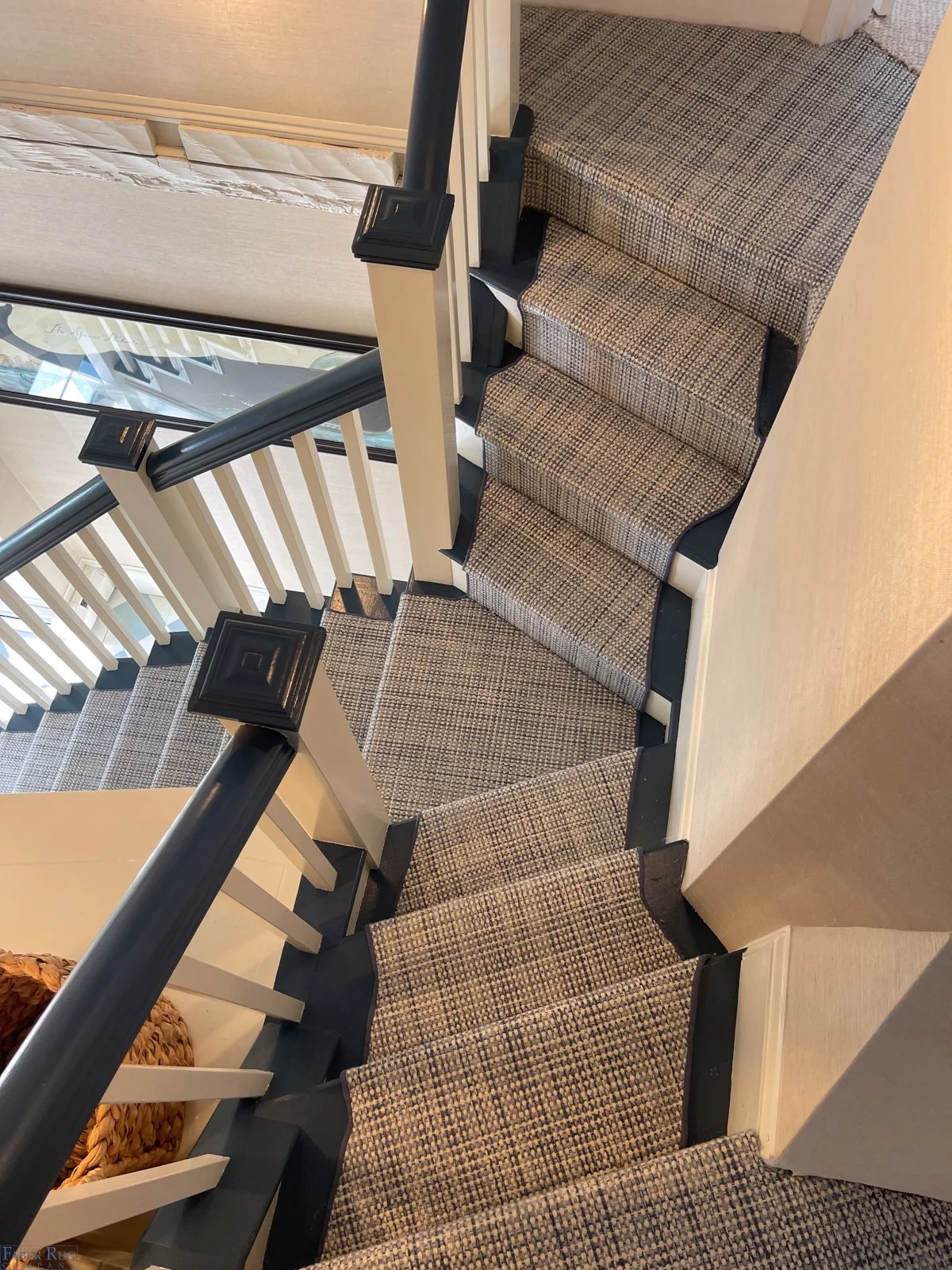 U-shaped staircase with carpeted steps, black railings, and white balusters, viewed from above.