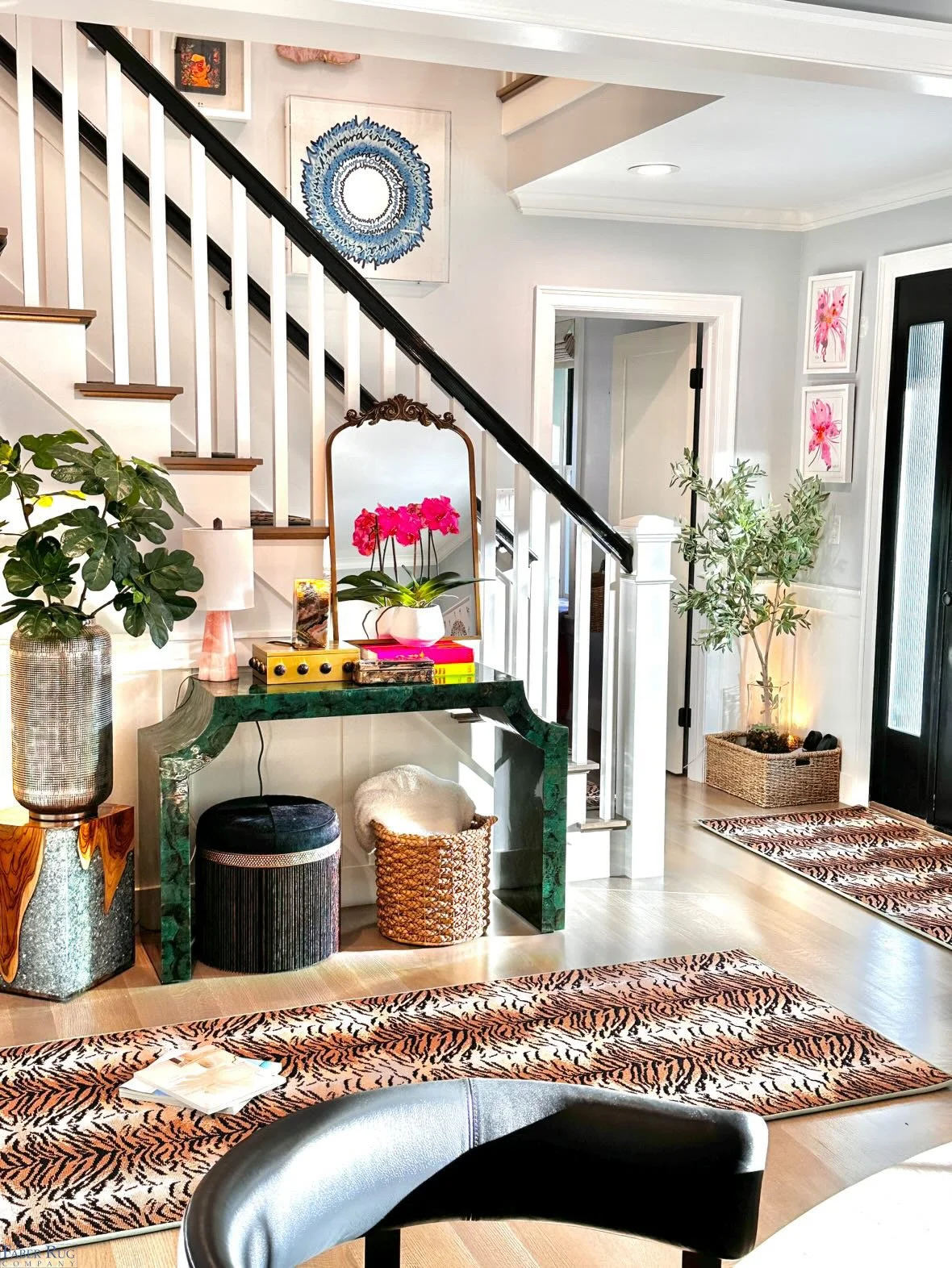 Decorated entryway with a staircase, plant, mirror, colorful artwork, and animal print rugs.